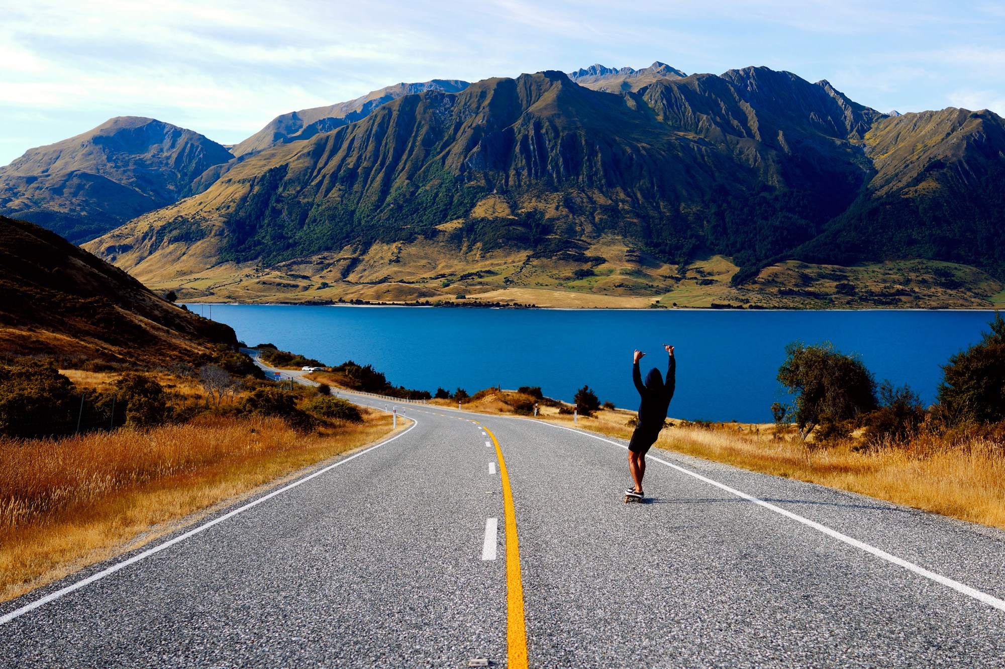 Kate Bellm photography: skateboarder skating downhill towards mountains and a lake