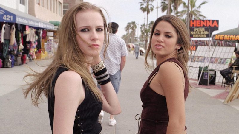 a still from the movie thirteen showing two women in black tank tops looking over their shoulders on a boardwalk