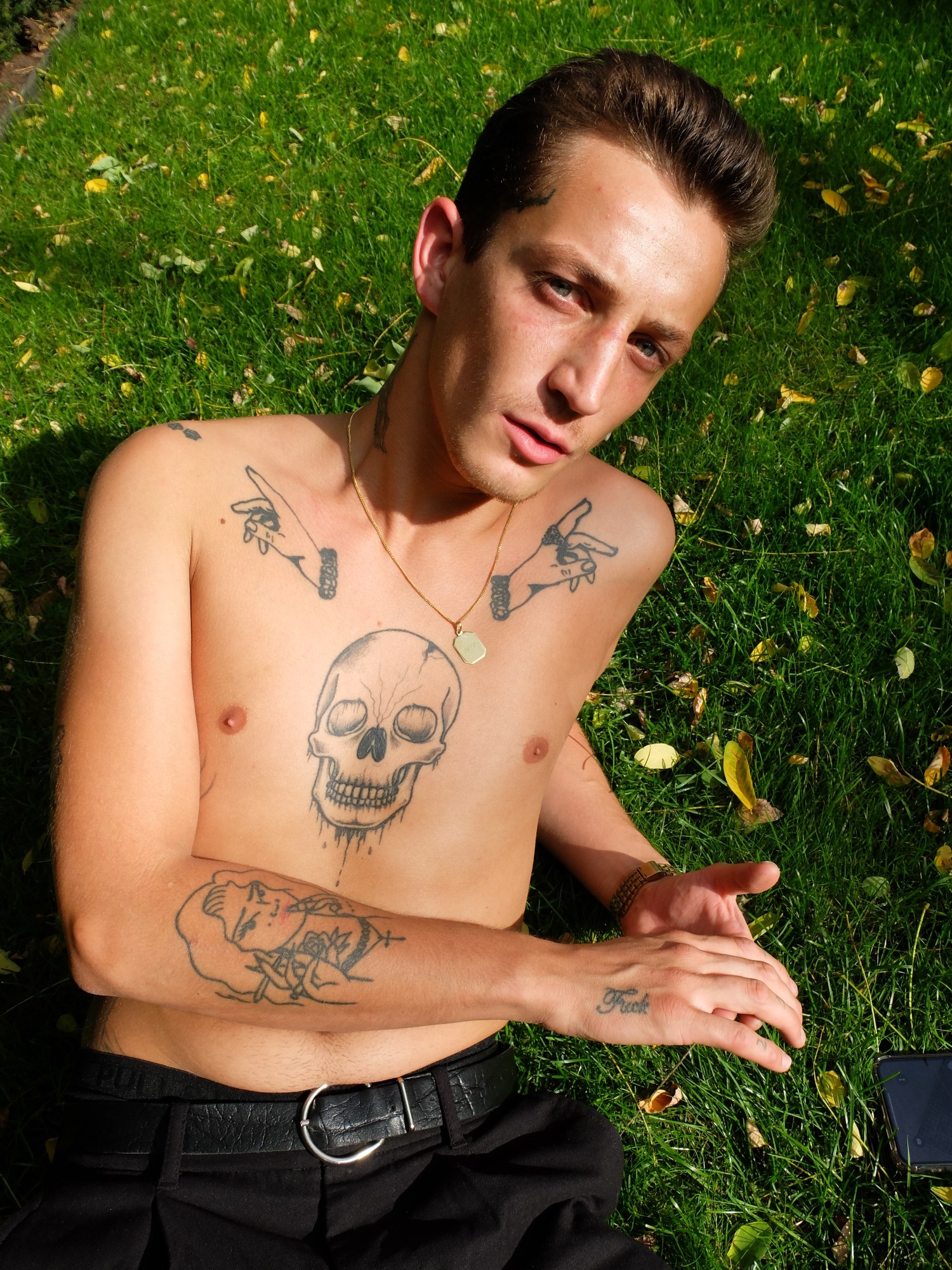 A topless, tattooed man reclines on a lawn.