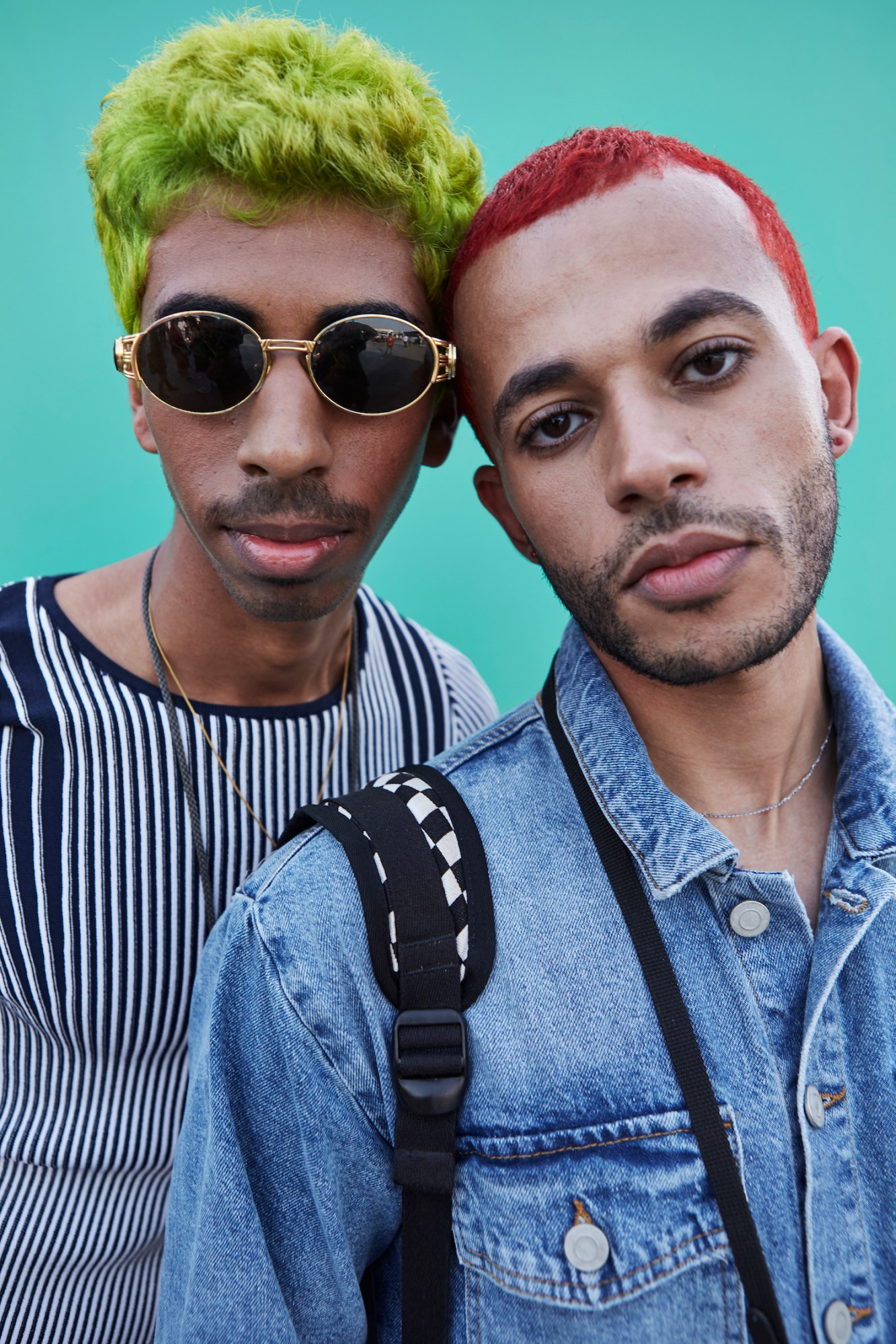 Two young men stare directly into the camera. The man on the left has green hair and wears sunglasses, the man on the left has short red hair.