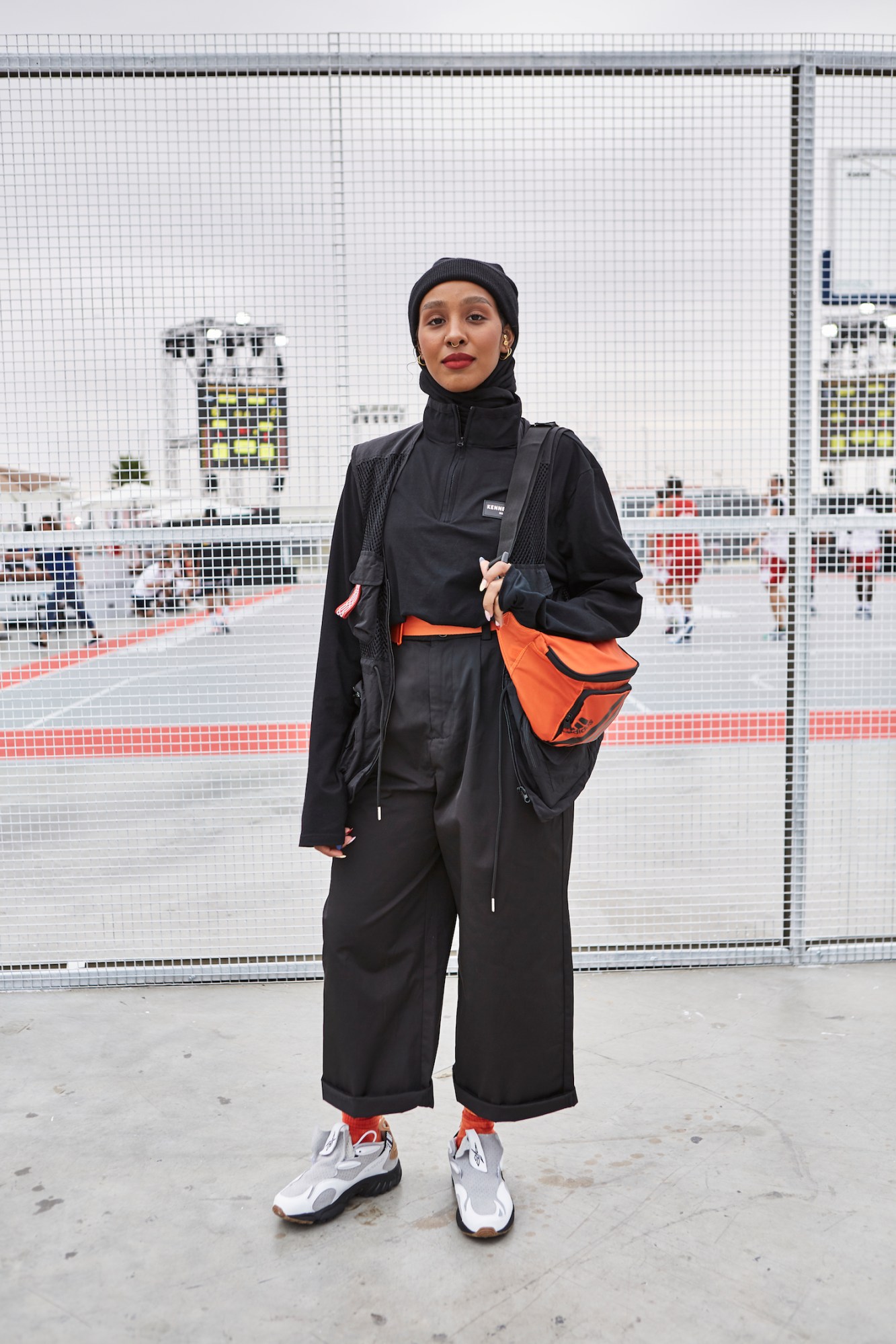 A woman wearing a hijab in black and orange streetwear look.