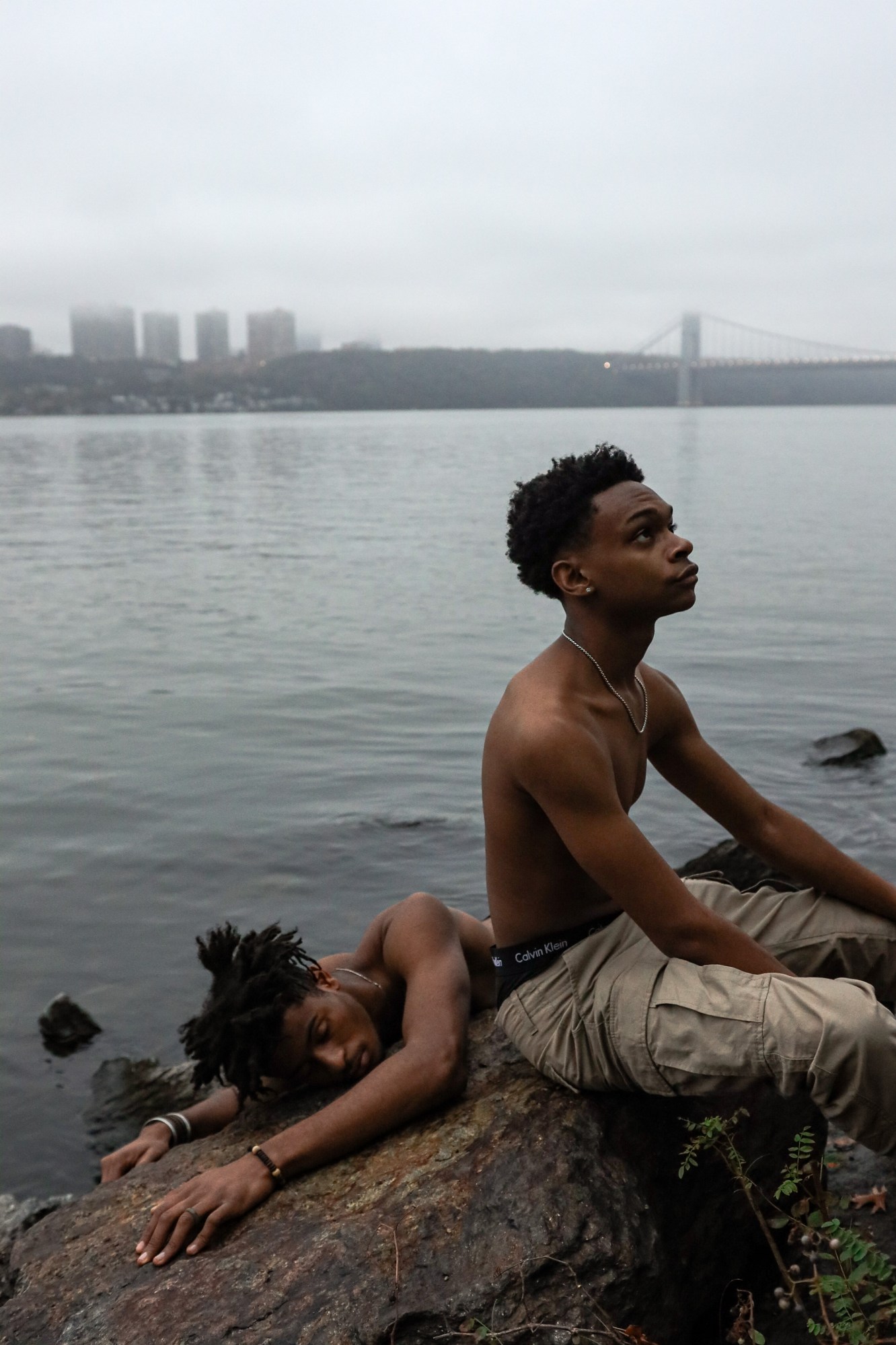 two men lying on a rock by a river