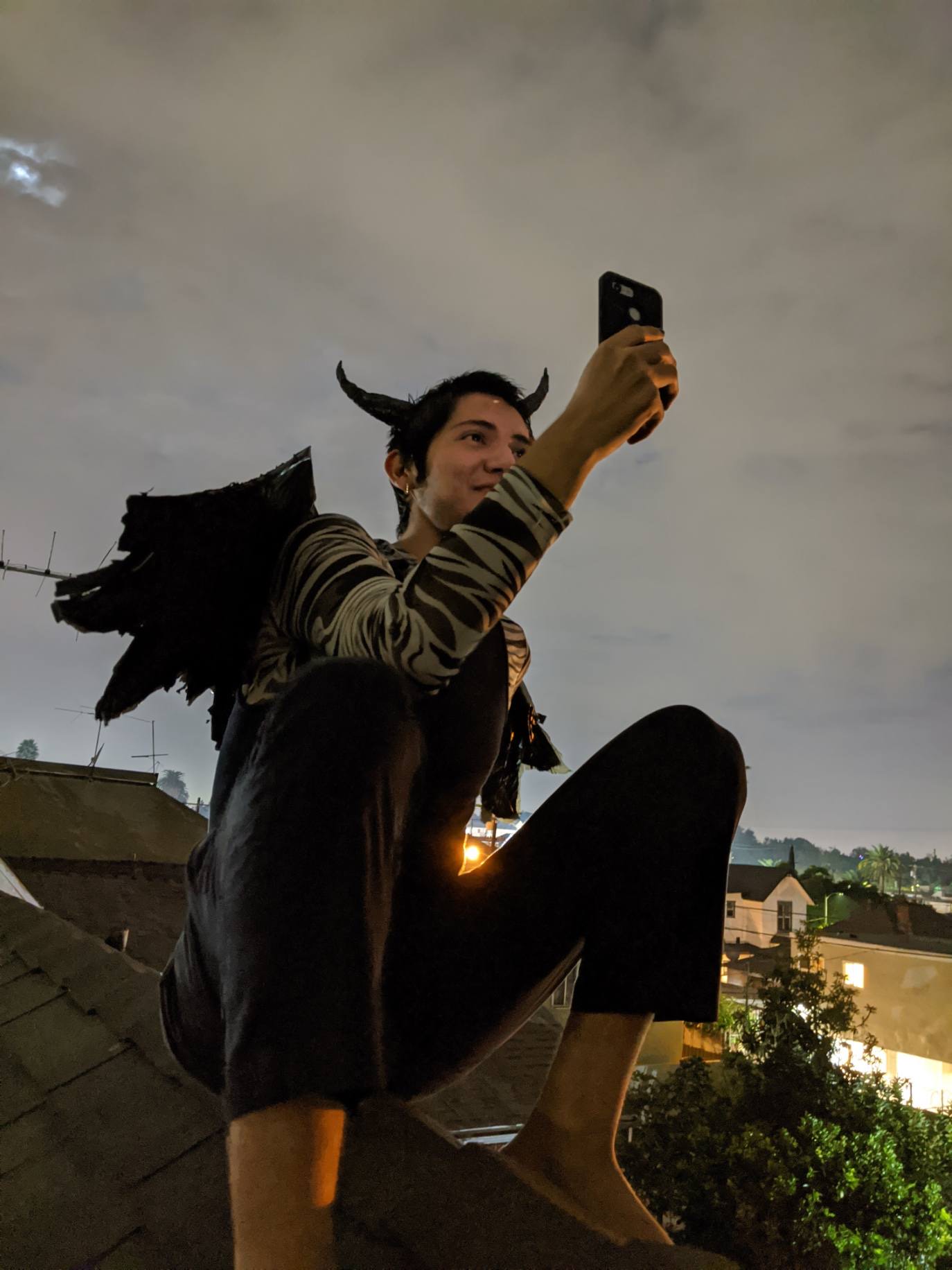 a man with wings sat on a roof trying to get phone signal