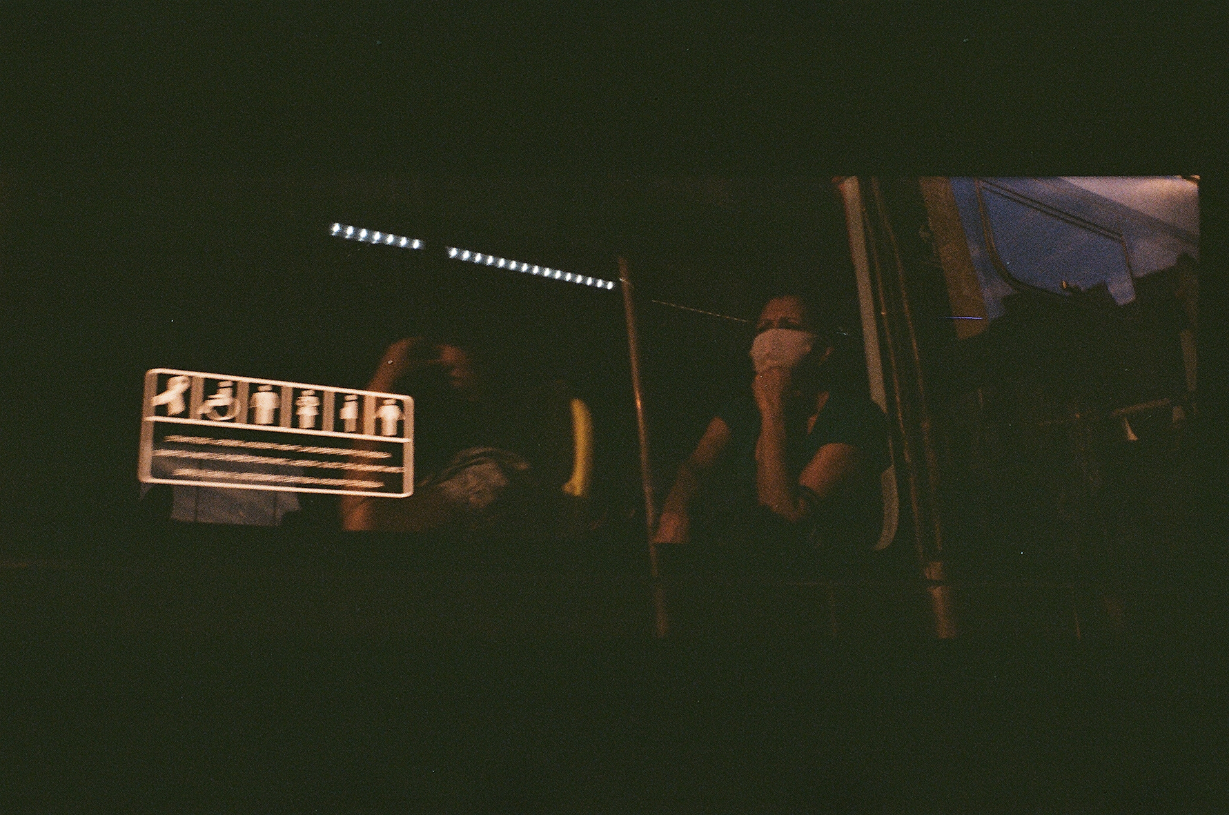 a woman on a bus with a face mask and the reflection of a public bathroom sign