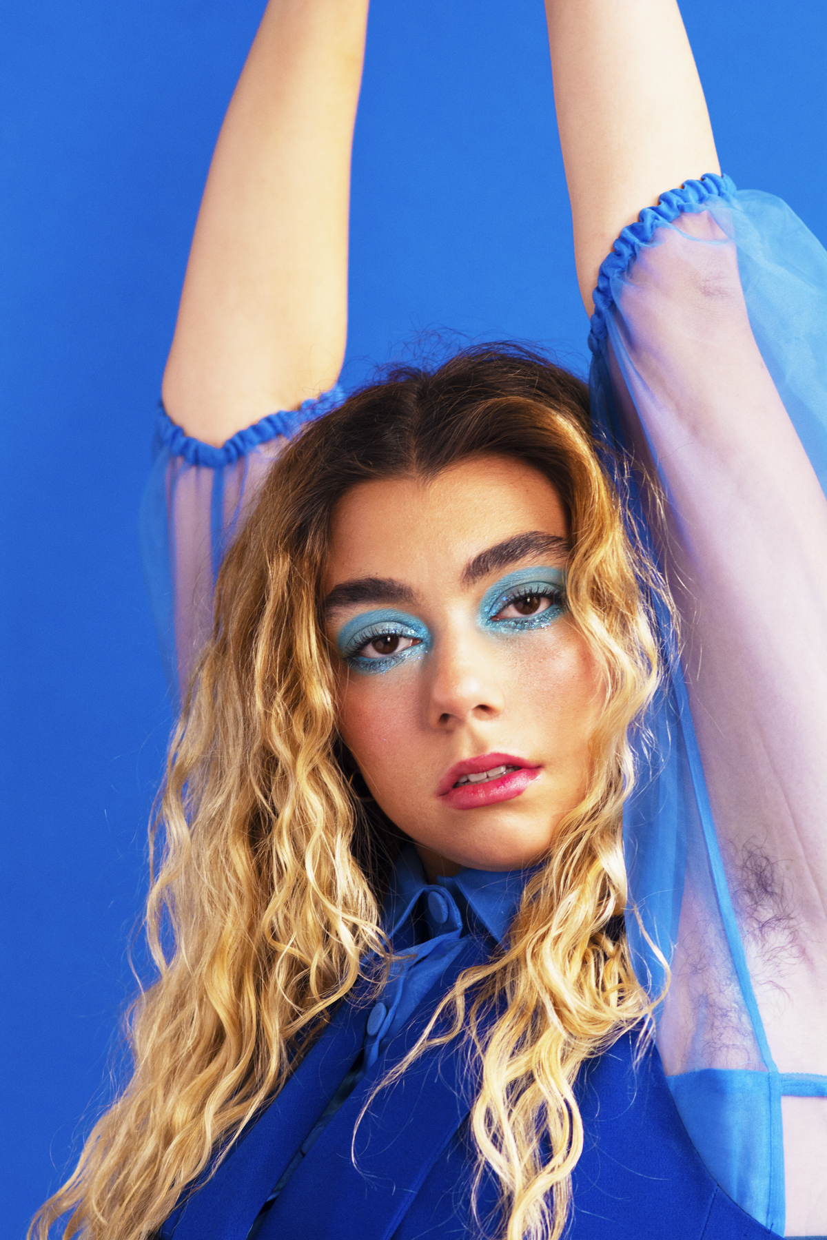 Woman with blue eyeshadow in a blue sheer blouse. Photographed by Marcus Branch.