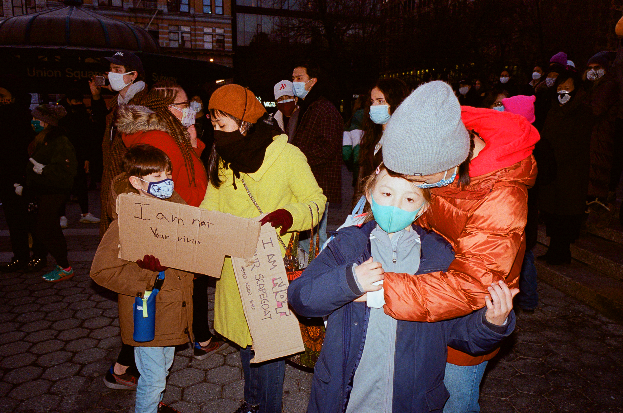 two woman and young children with signs, one that reads 'i am not your virus' at the asian peace vigil in new york