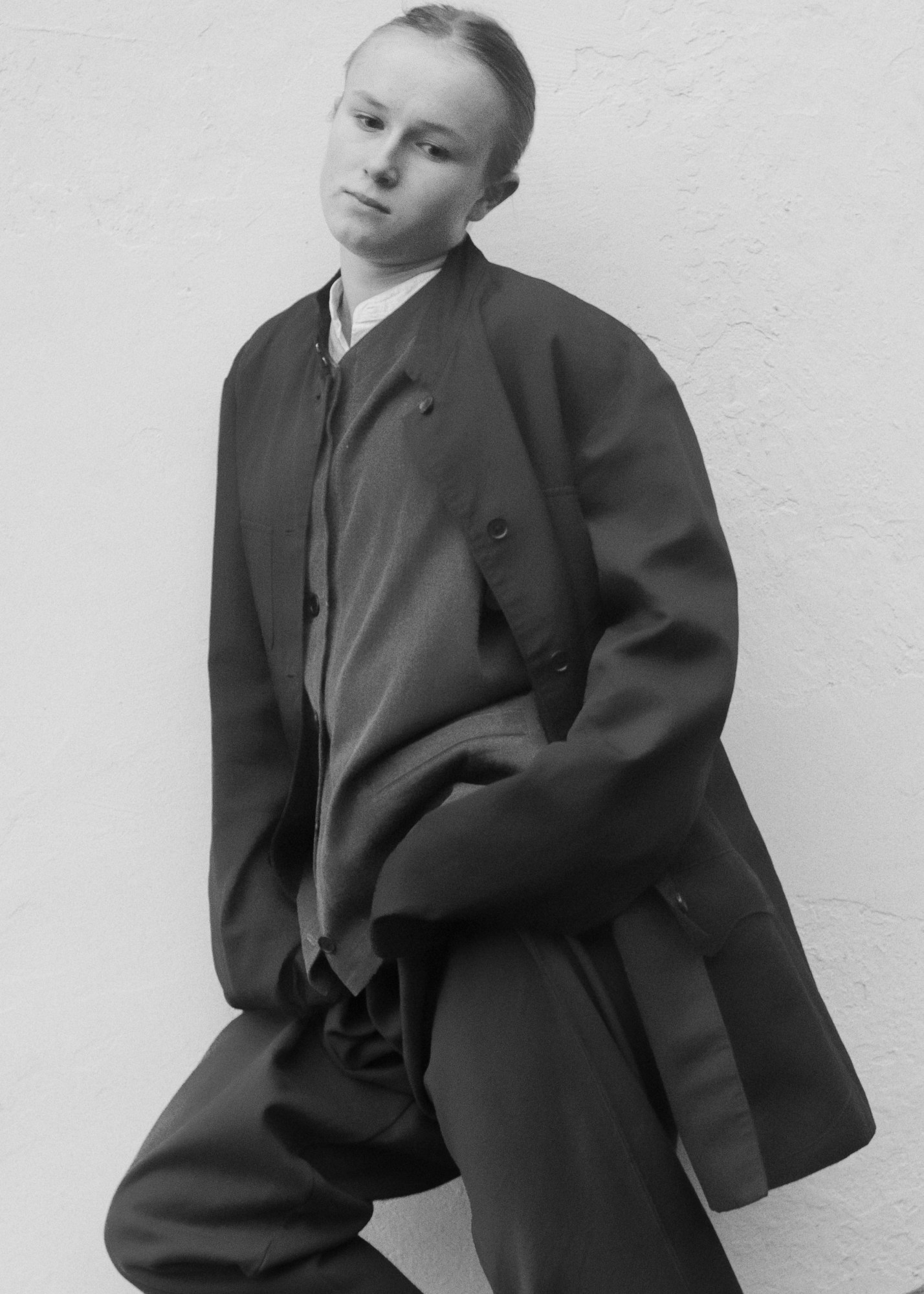 a girl wearing formal black attire against a white wall