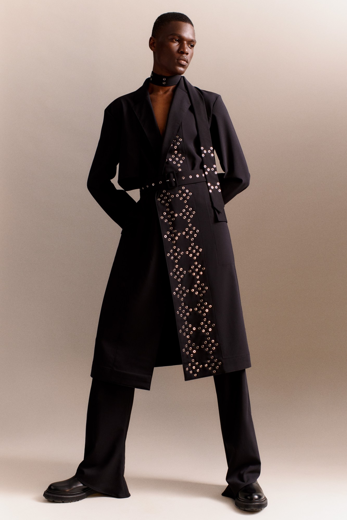 Ludovic de Saint Sernin AW21 – model wearing a black coat decorated with eyelets in a diamond pattern