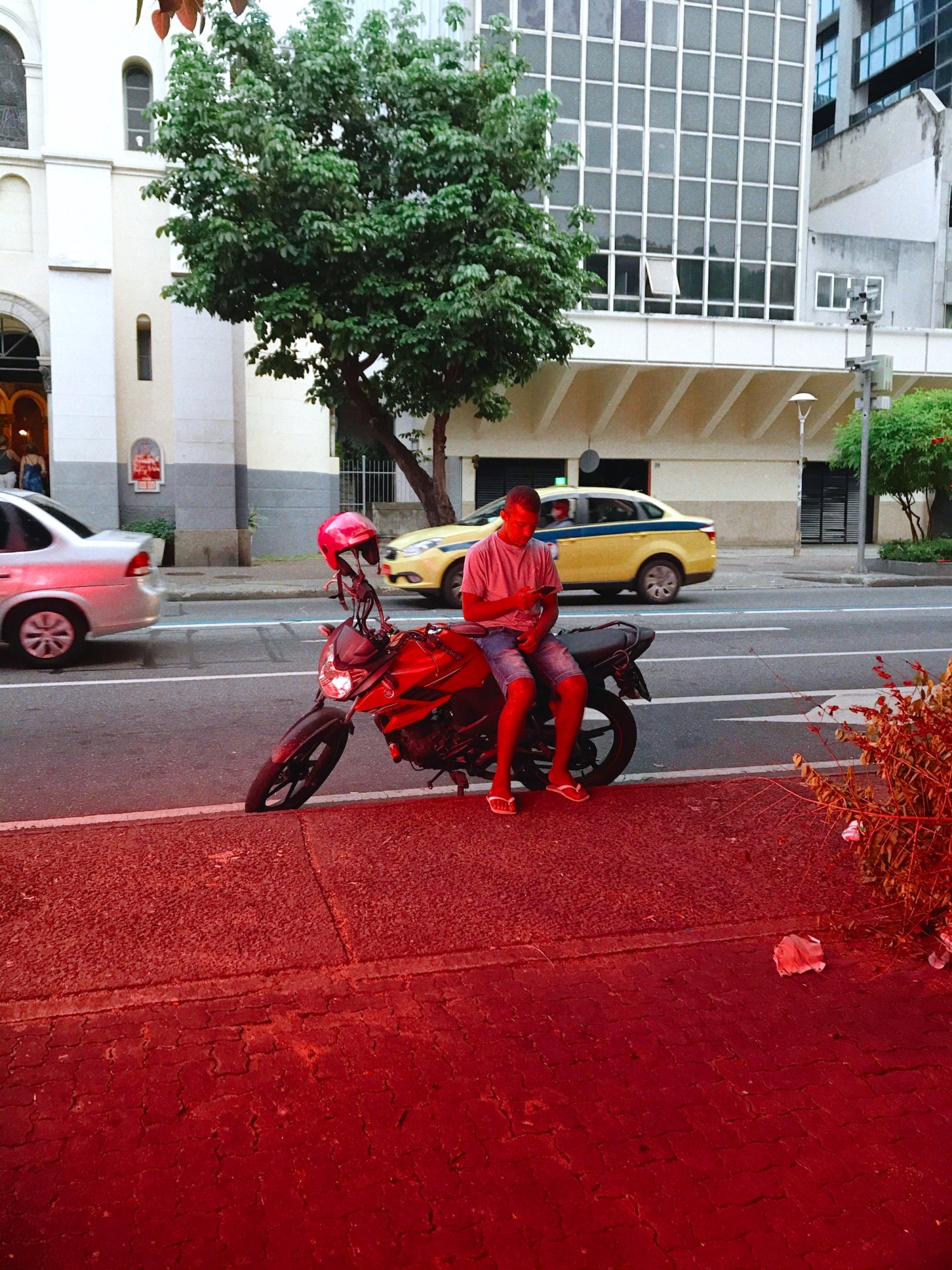 a man sits on a motorbike on the side of the road, covered in red light