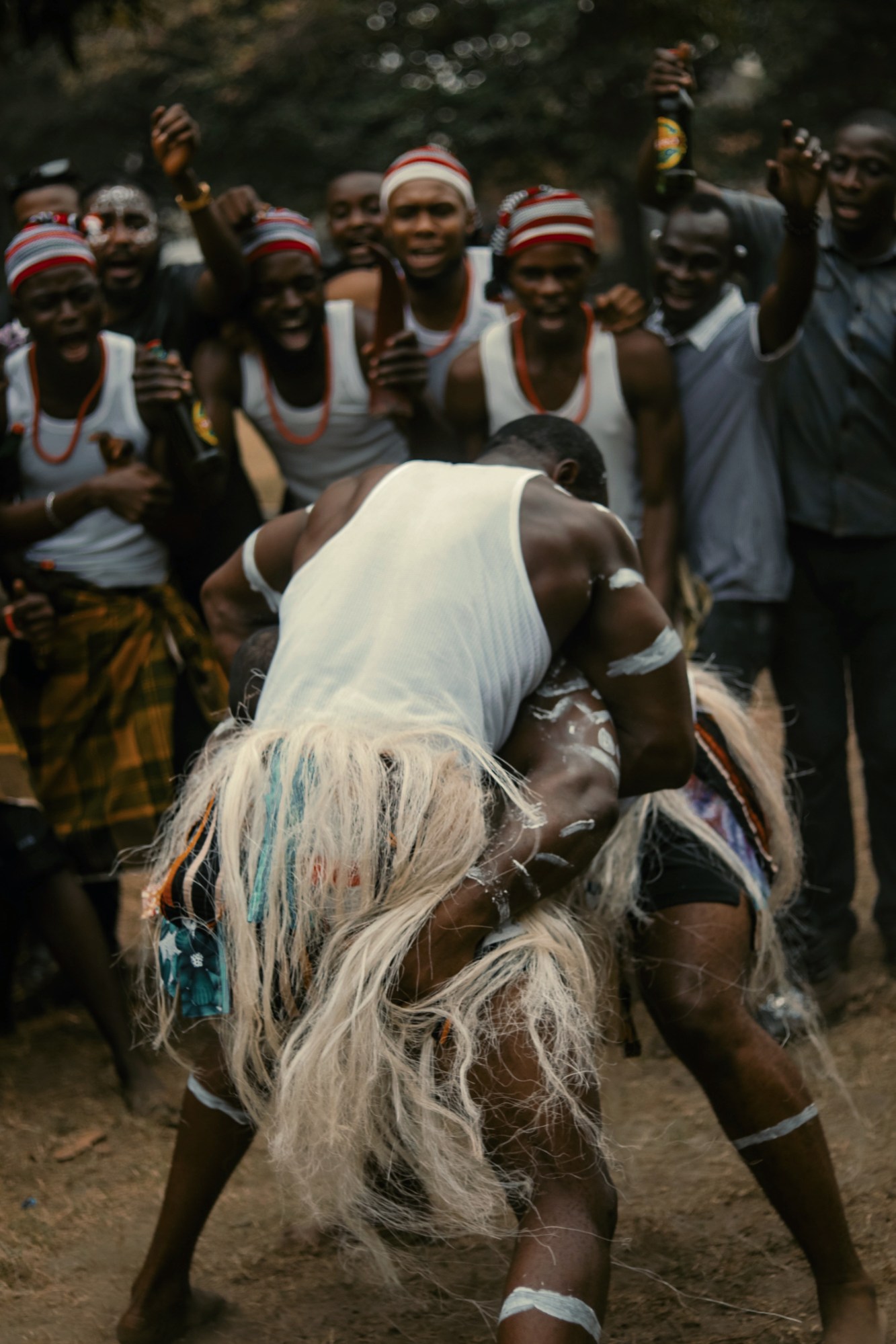 two nigerian men fight with painted marks on their skin as a group of men cheer and shout around them