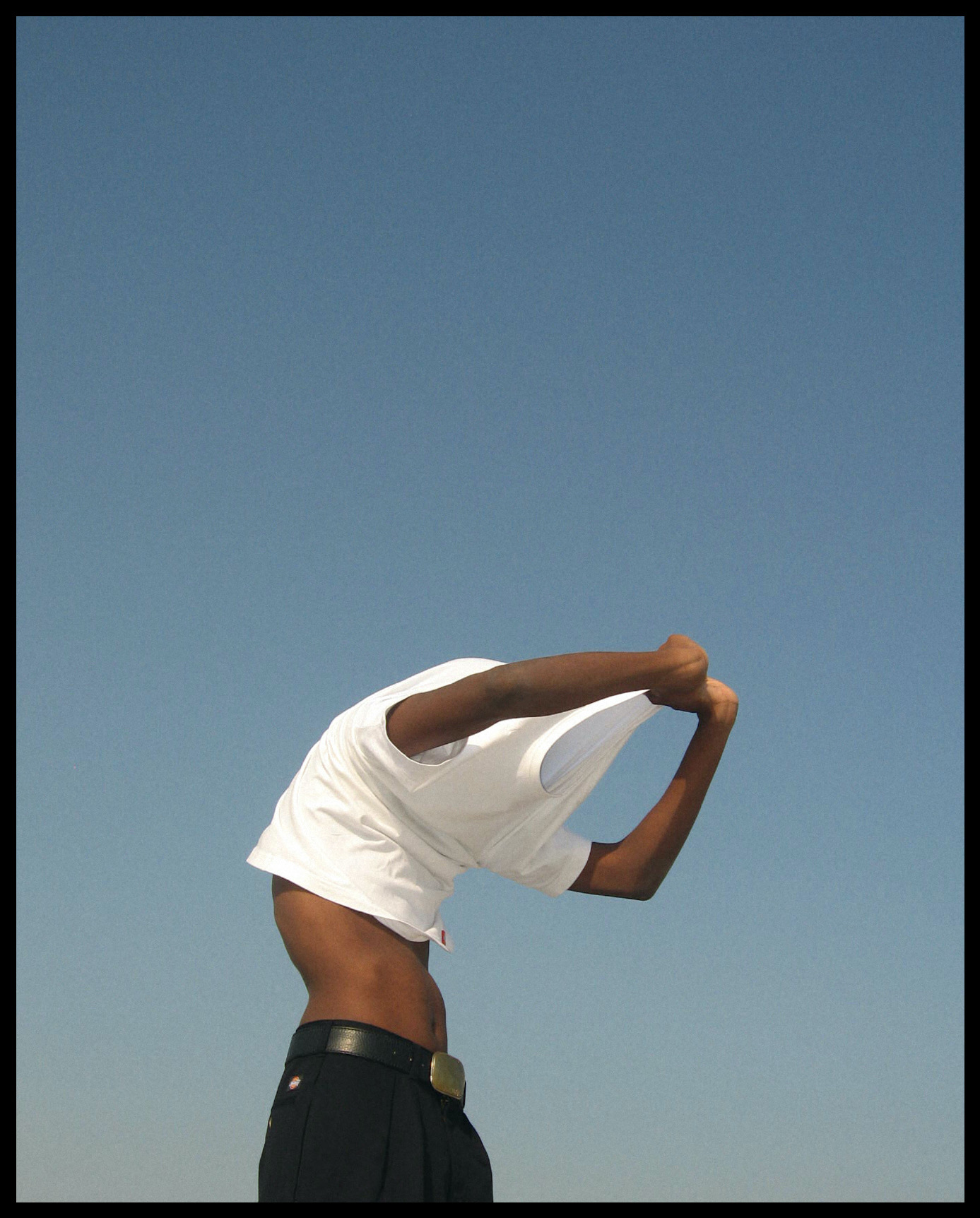 a man pulls off a white t-shirt in front of a light blue sky