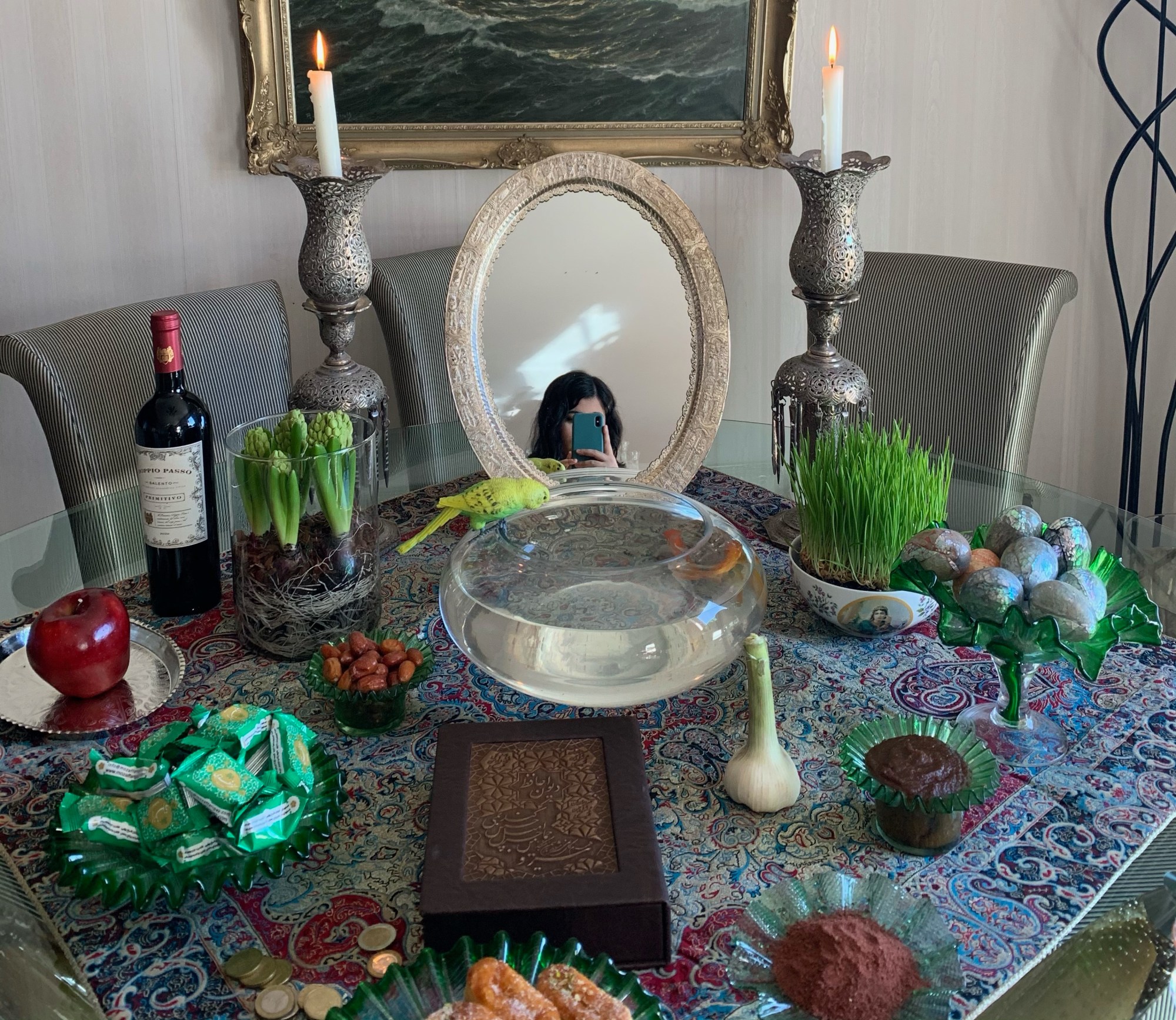 a woman takes a selfie in a mirror on a table that is surrounded by different plants, bottles, candle sticks and food