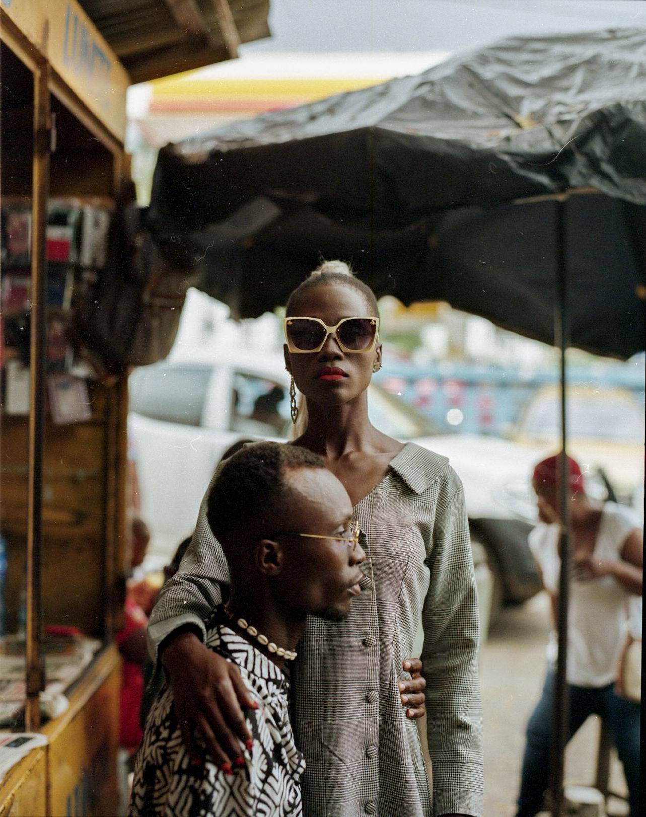 a man sits and a woman in sunglasses stands in front of a street food vendor