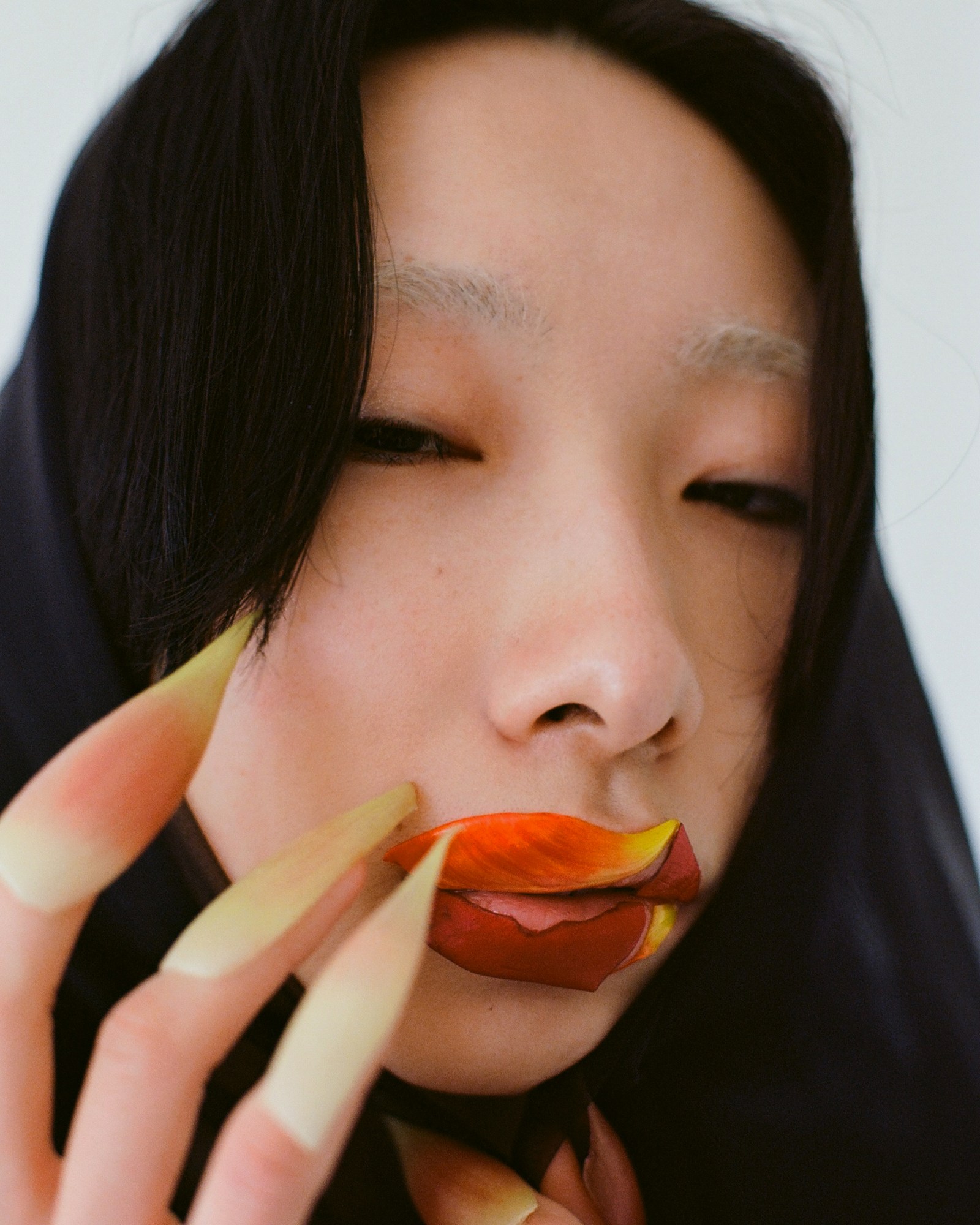 a woman with bleached eyebrows and petals over her nails and lips