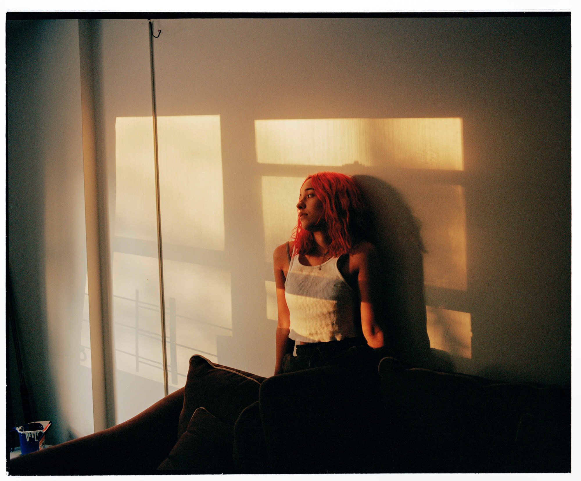 a girl with pink hair sits against the wall in shadows cast of a sunset