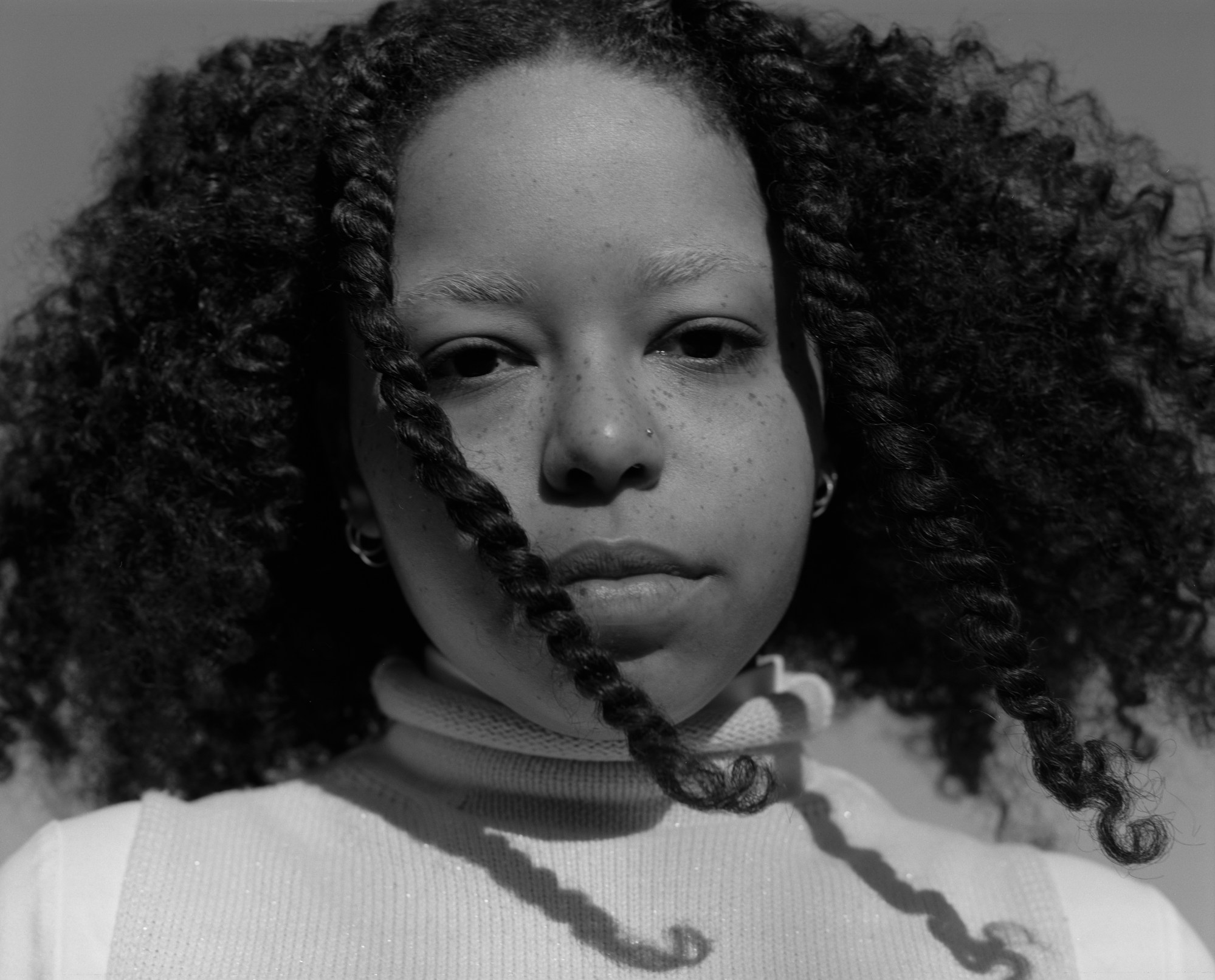 a girl with freckles, bleached eyebrows and thick black curly hair stares into the camera