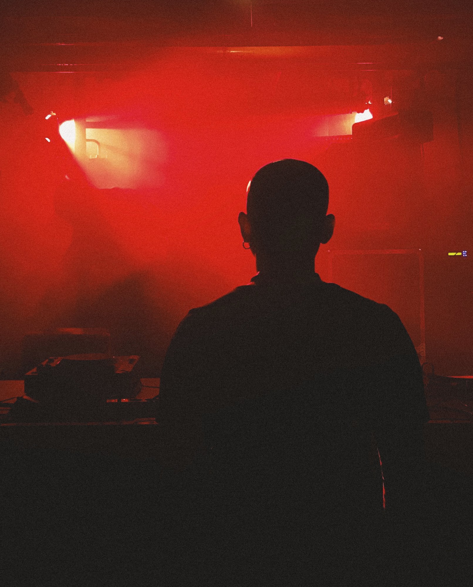 the silhouette of a man at dj deks in an empty club filled with red light