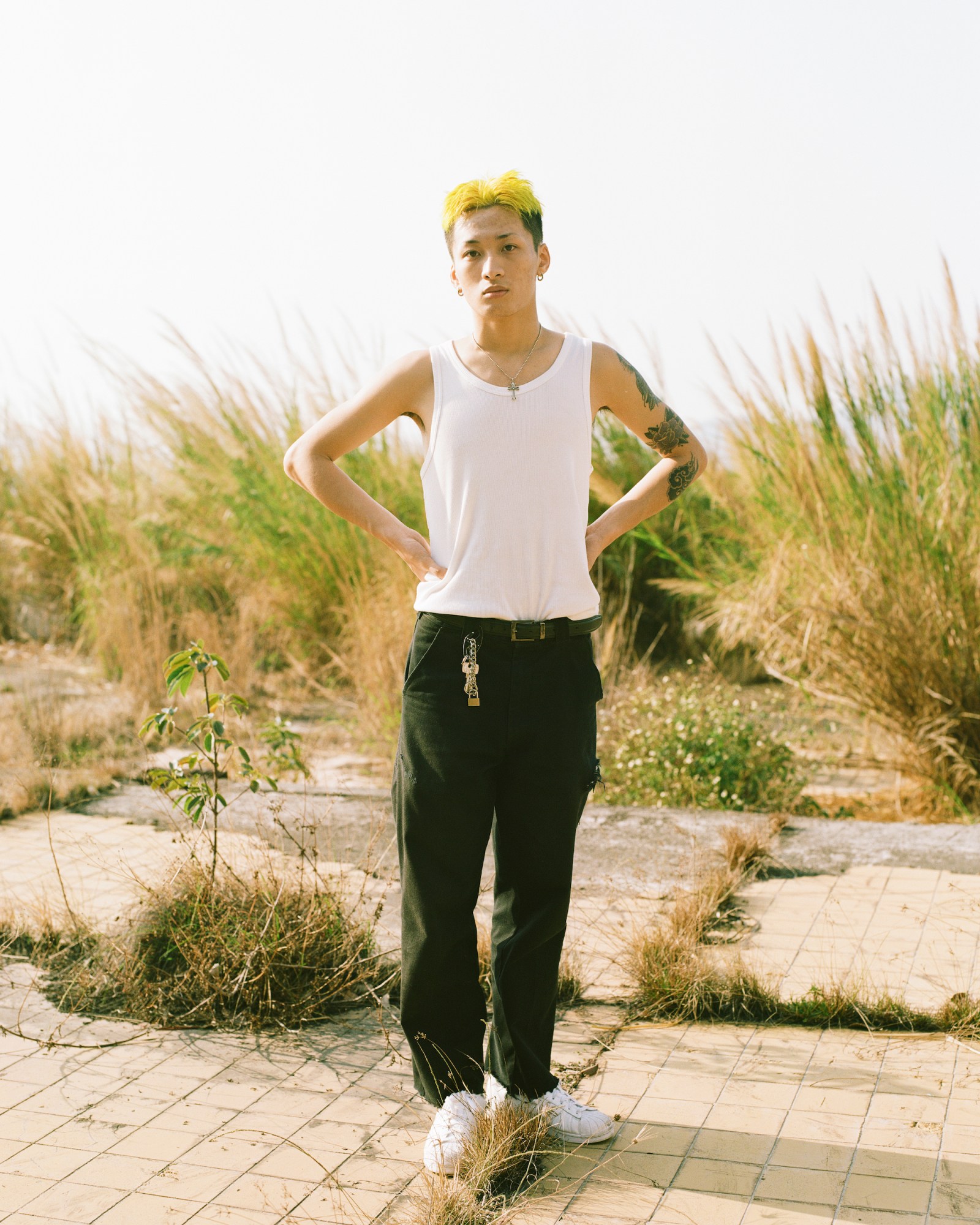 a man in a white vest with green hair stood in front of long grass