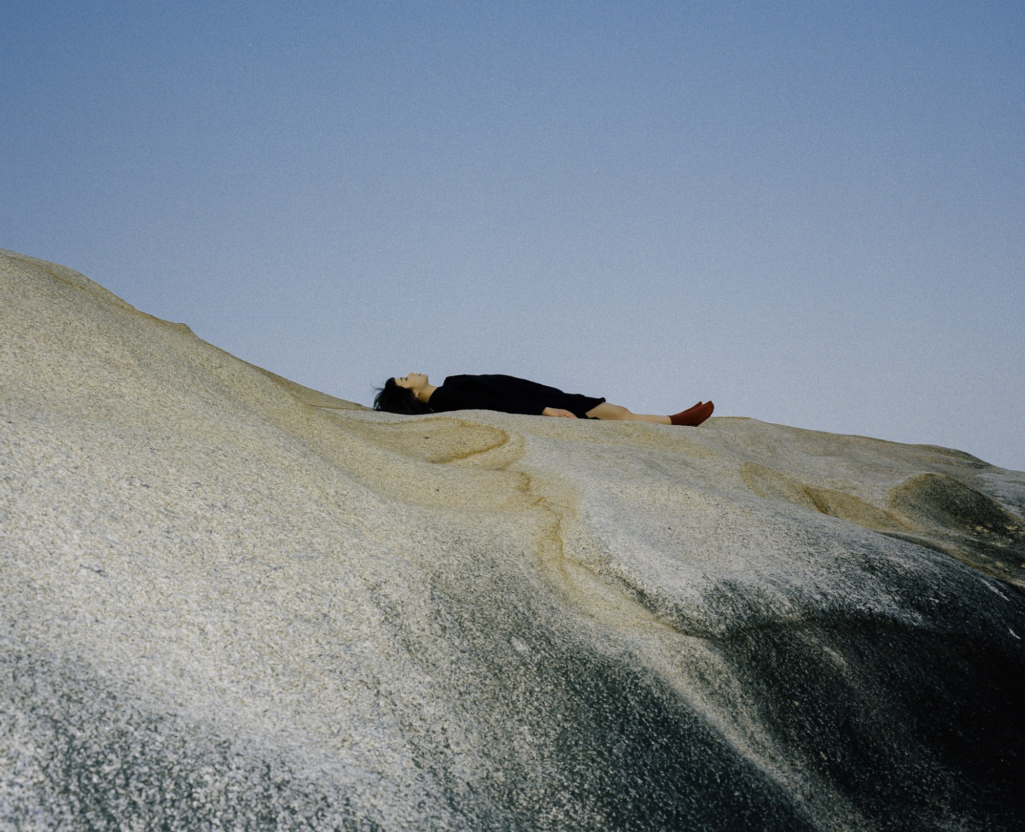 a person wearing all black lies on a rock