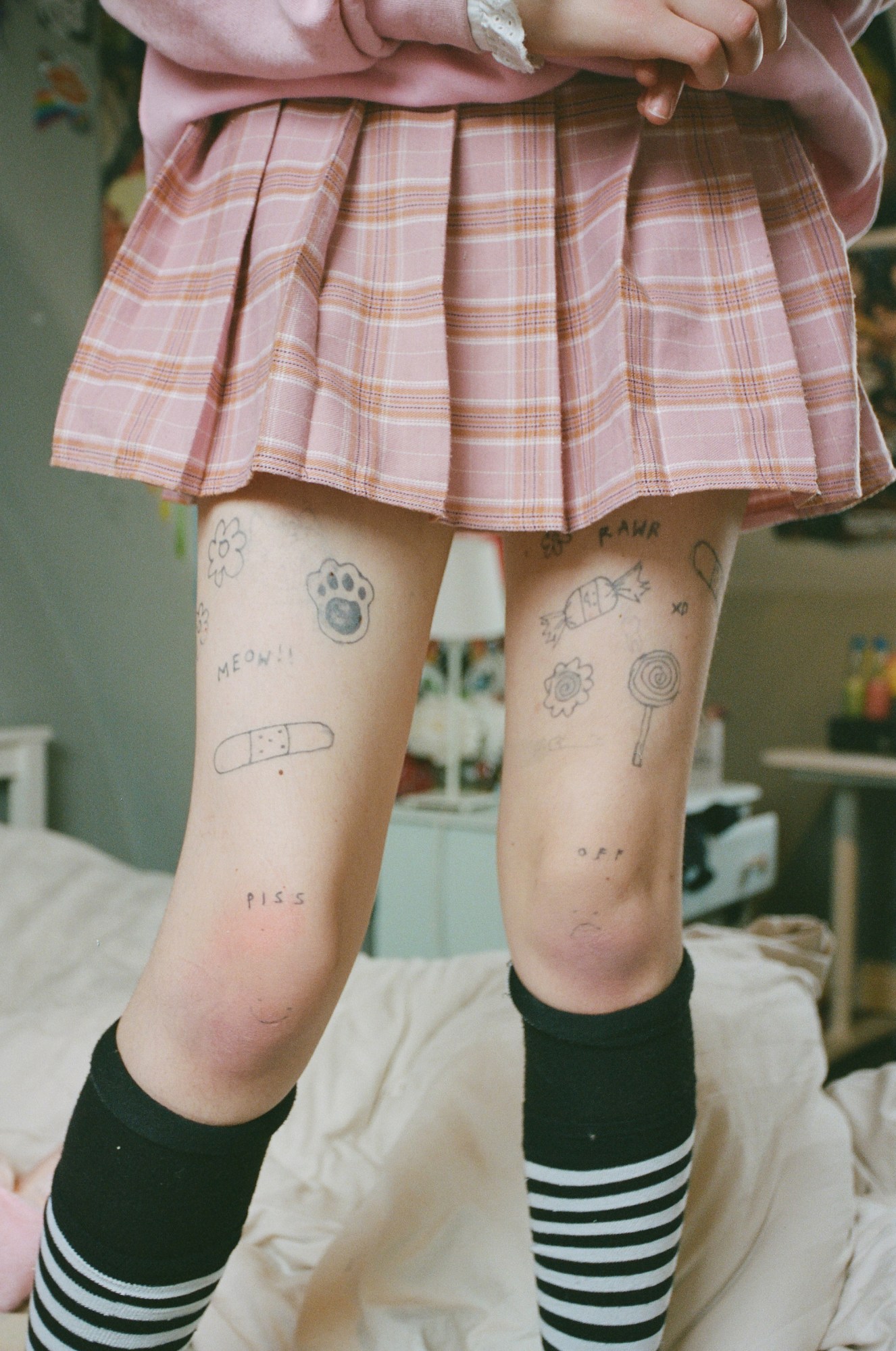 a girl's legs are covered in tattoos, reading piss off across both legs, as well as various pictures of flowers, footprints, lollipops and more