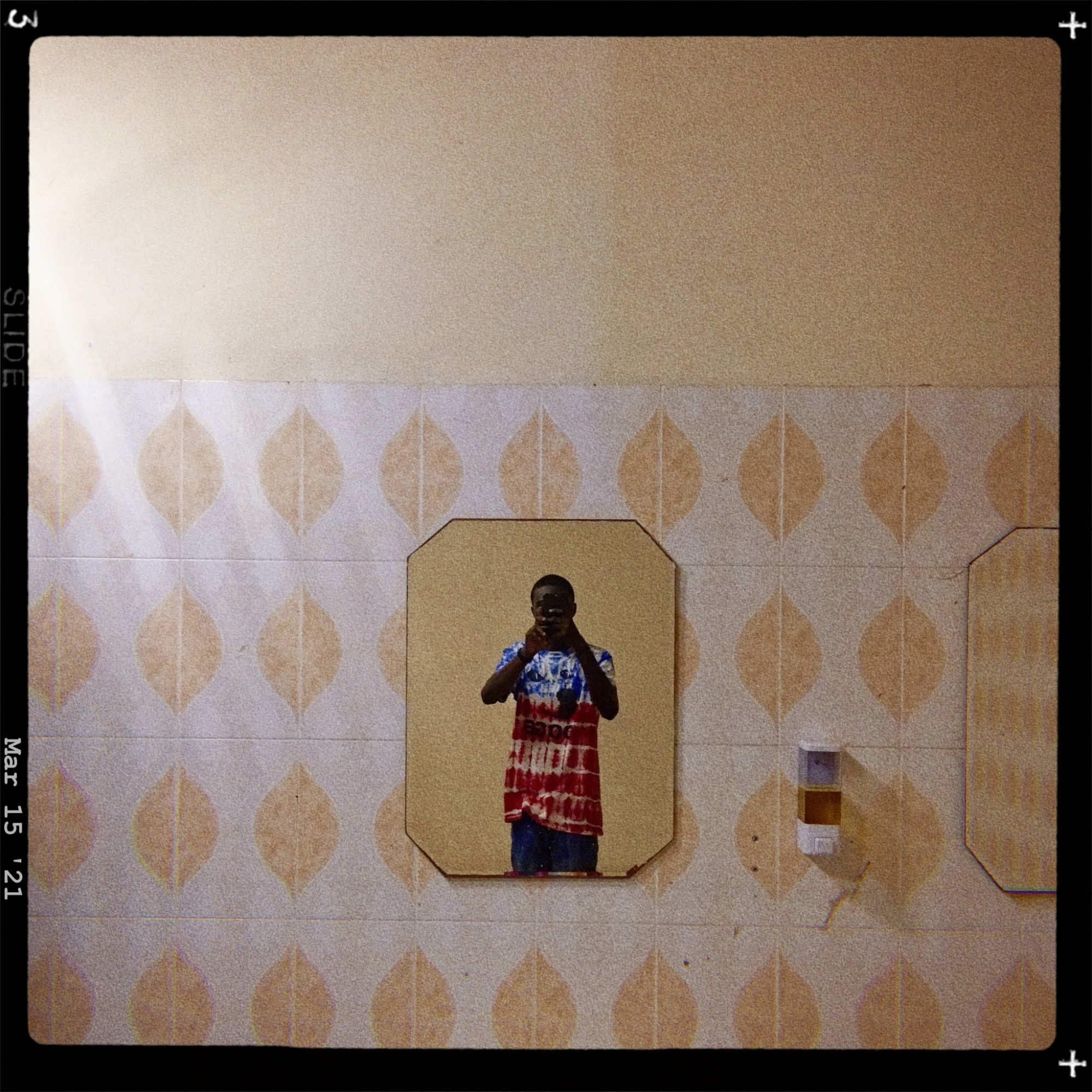 a man takes a selfie in a mirror, wearing a red and blue tie dye top