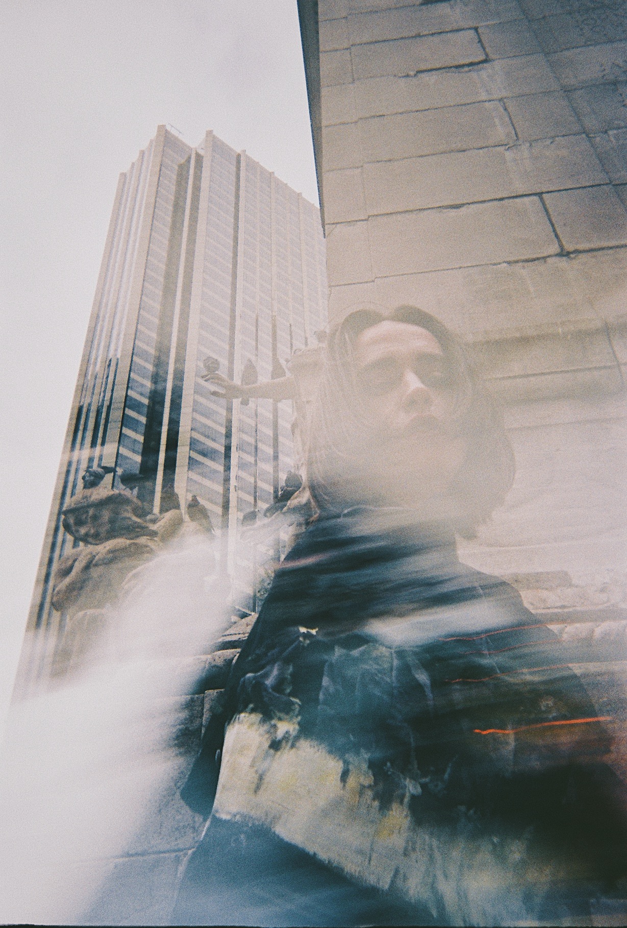 a blurry woman looks into the camera, a skyscraper can be seen behind her