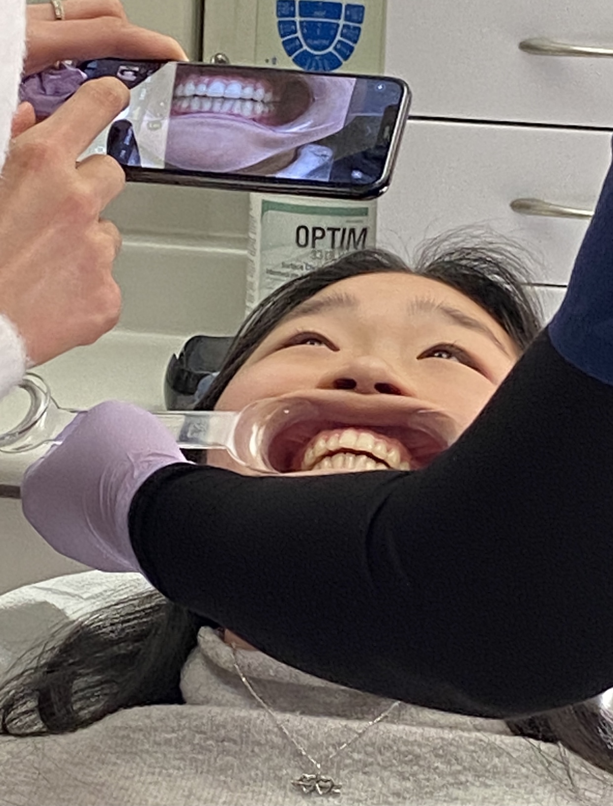 a woman has her mouth held open by a dentist, as a person takes a picture of her teeth