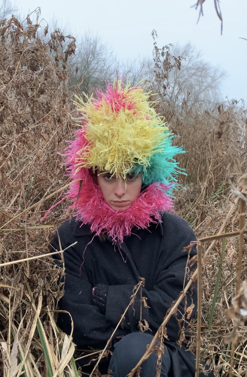 a woman sits in a field of dead leaves wearing a brightly coloured headdress