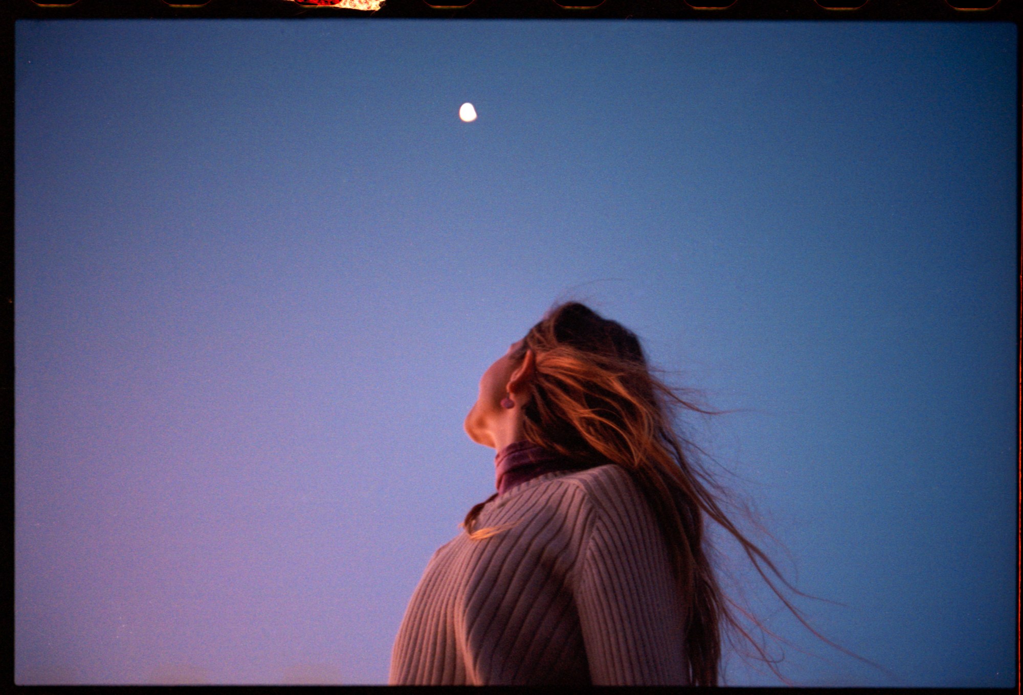 a woman stares up at the moon in a purple blue sky