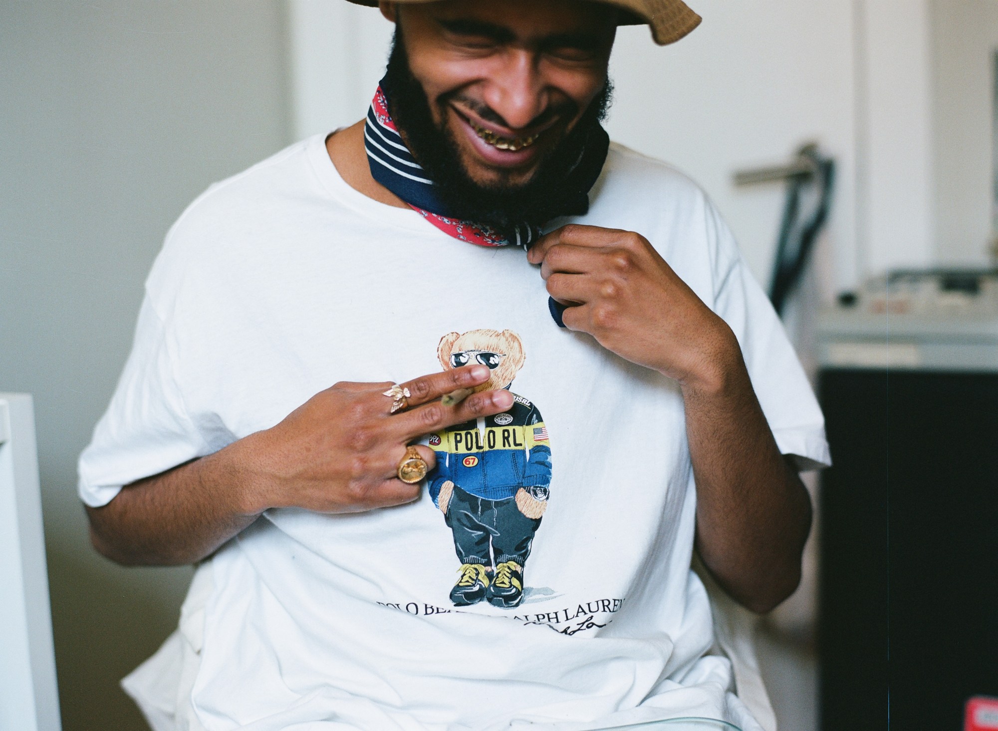 A laughing man holds a cigarette up to the bear illustrated on his t-shirt