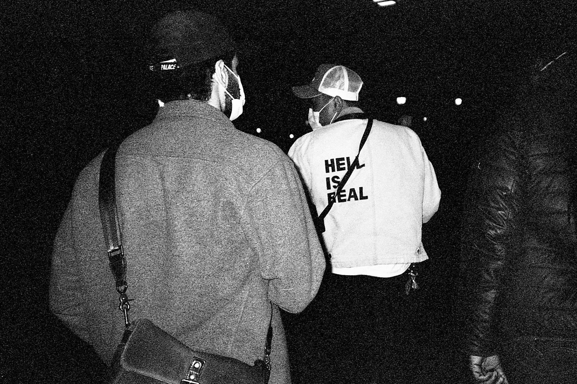 the backs of three men, one of whom wears a jacket that says 'hell is real'