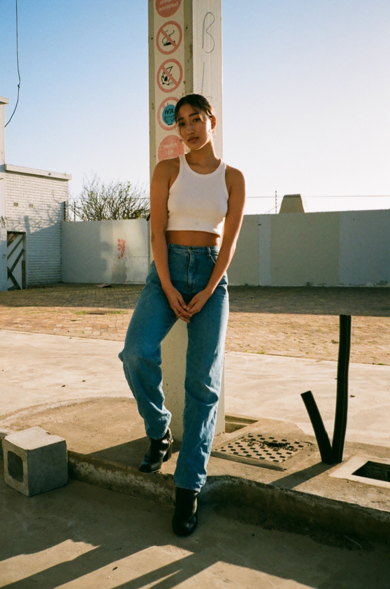 a woman wearing high rise blue jeans and a white top standing against a concrete pillar