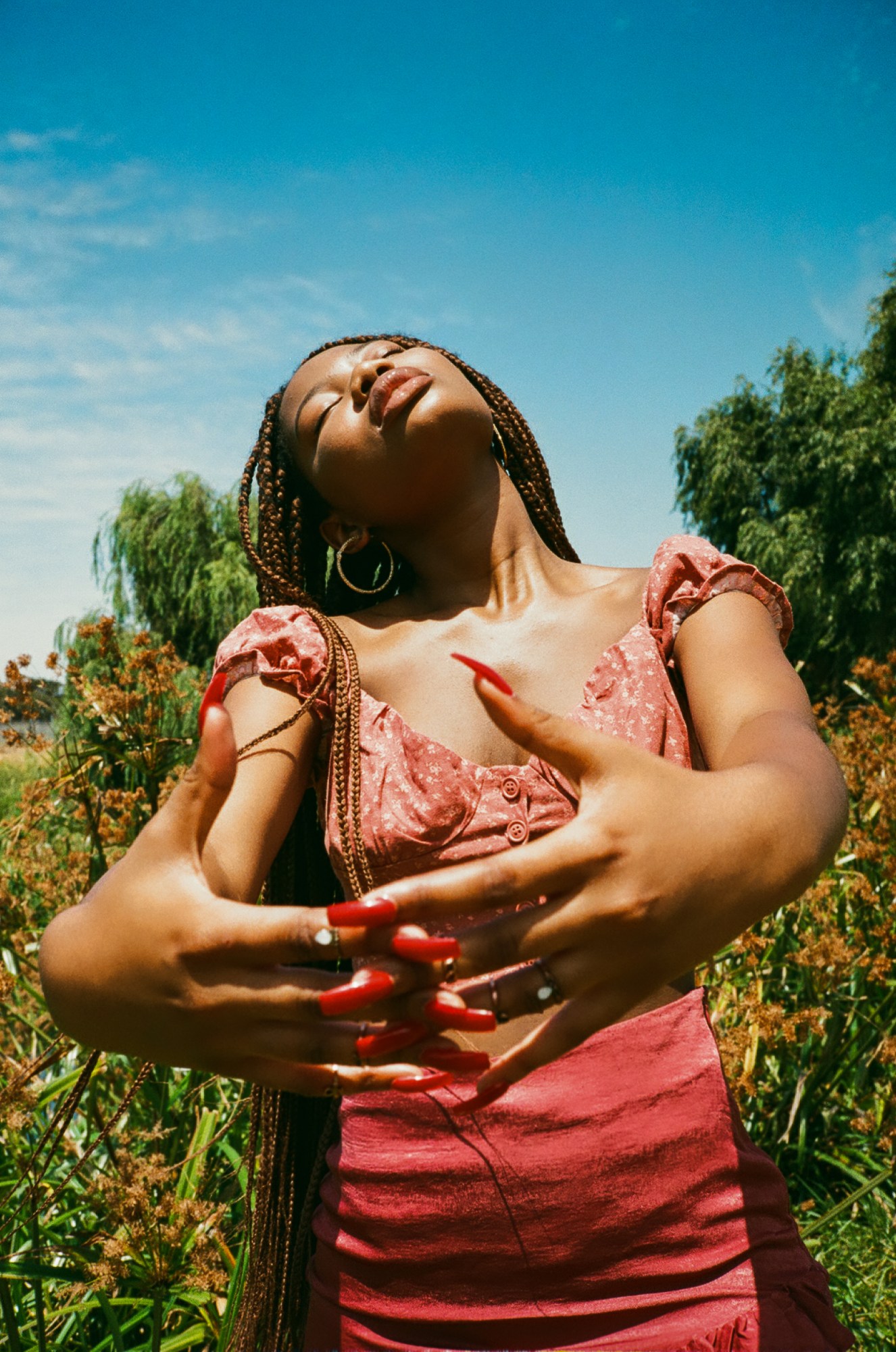 a woman with long red nails holds her hands together and faces up towards the sky