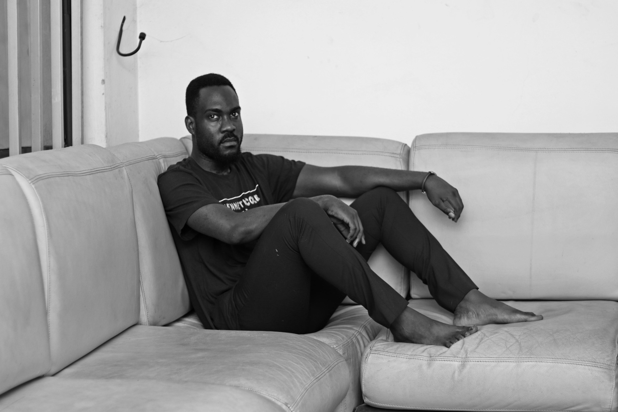 a man sits in the corner of a sofa staring into the camera