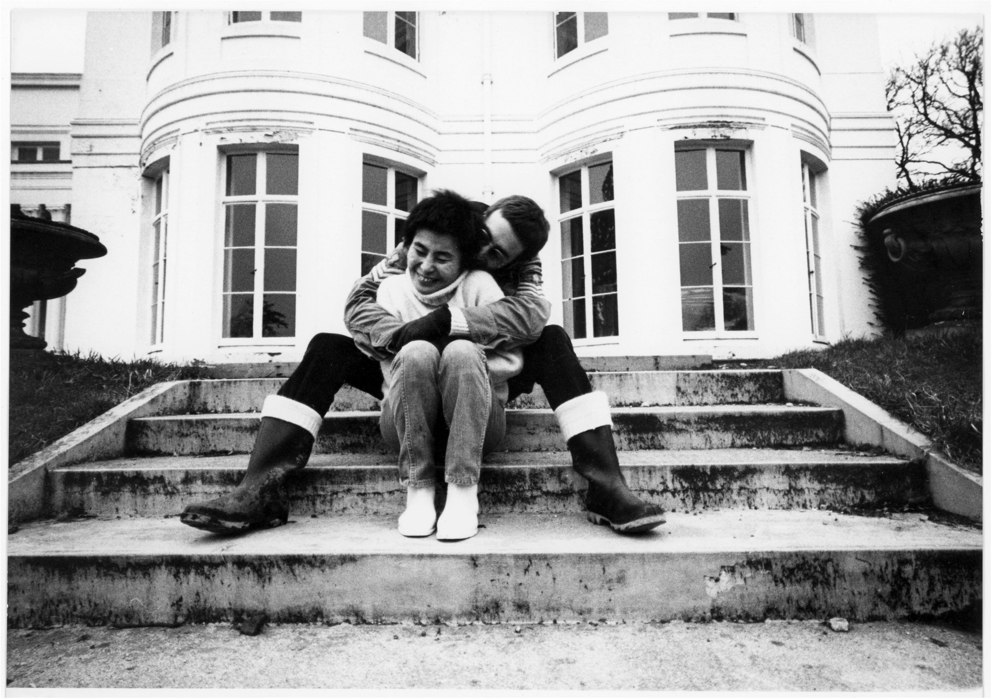 Yoko Ono and John Lennon sitting playfully on some steps outside their home