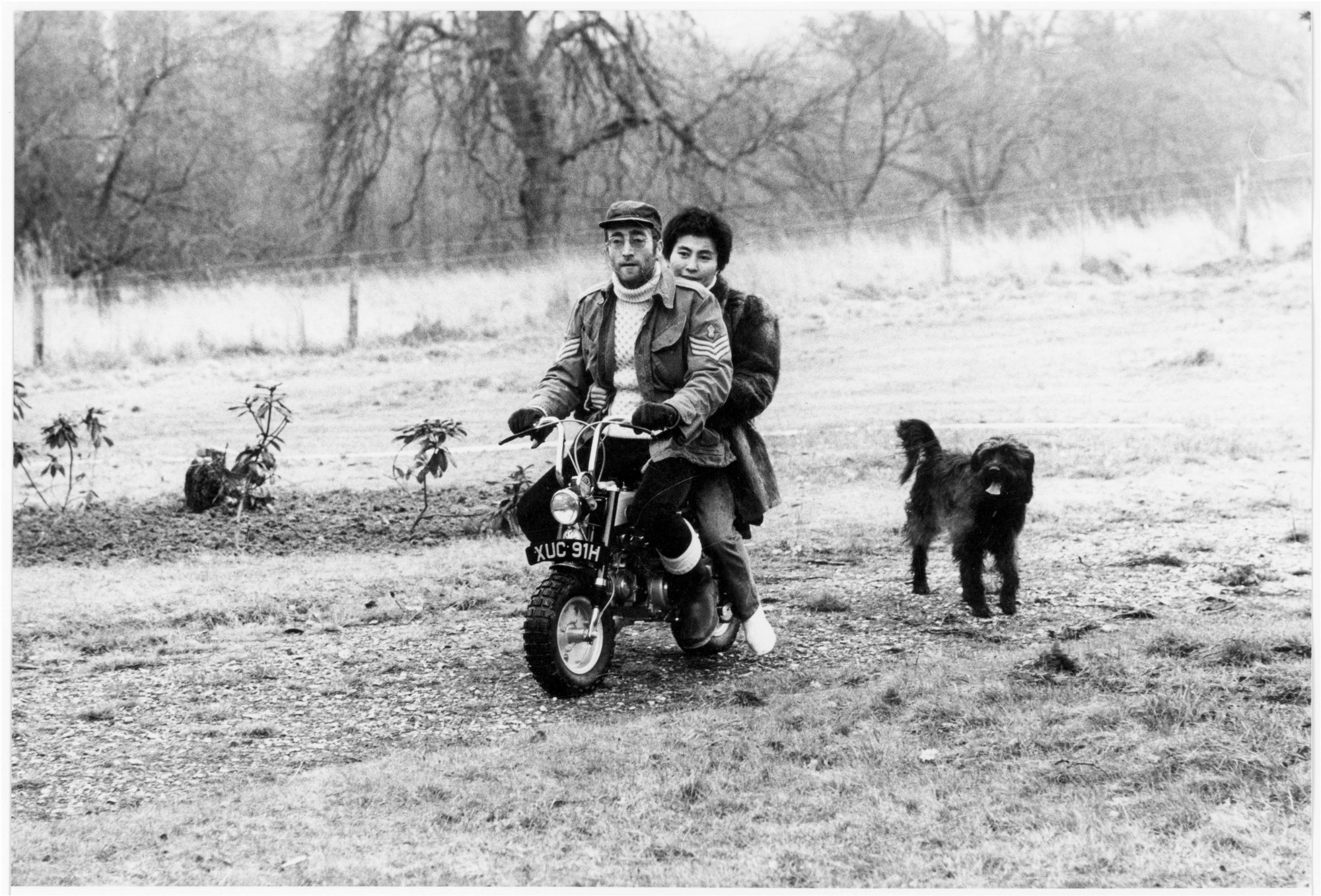 Yoko Ono and John Lennon riding a mini motorbike around their garden, followed by a black dog