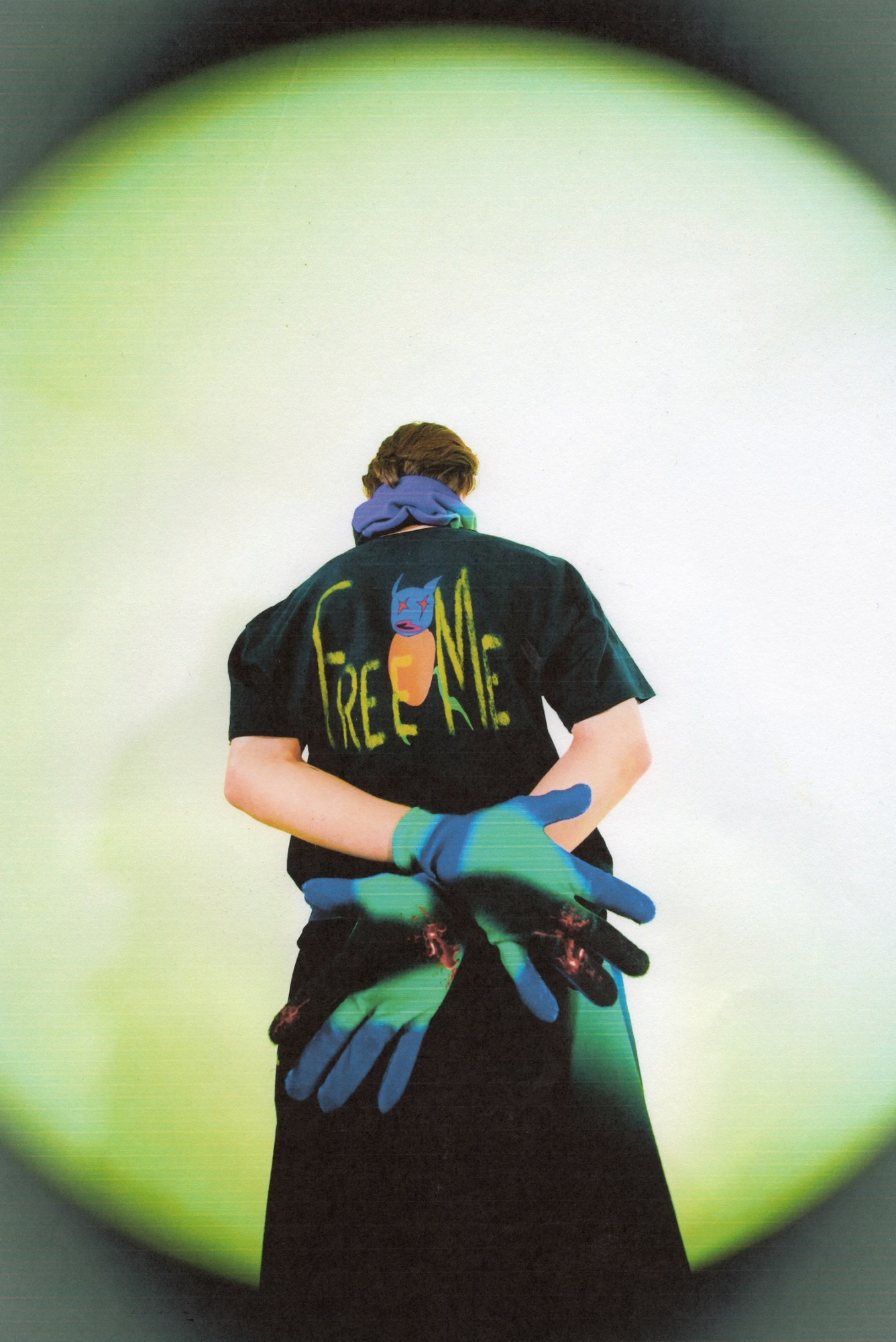 A man with his hands crossed behind his back, wearing tie-dye gloves and a black t-shirt with 'free me' printed on it.