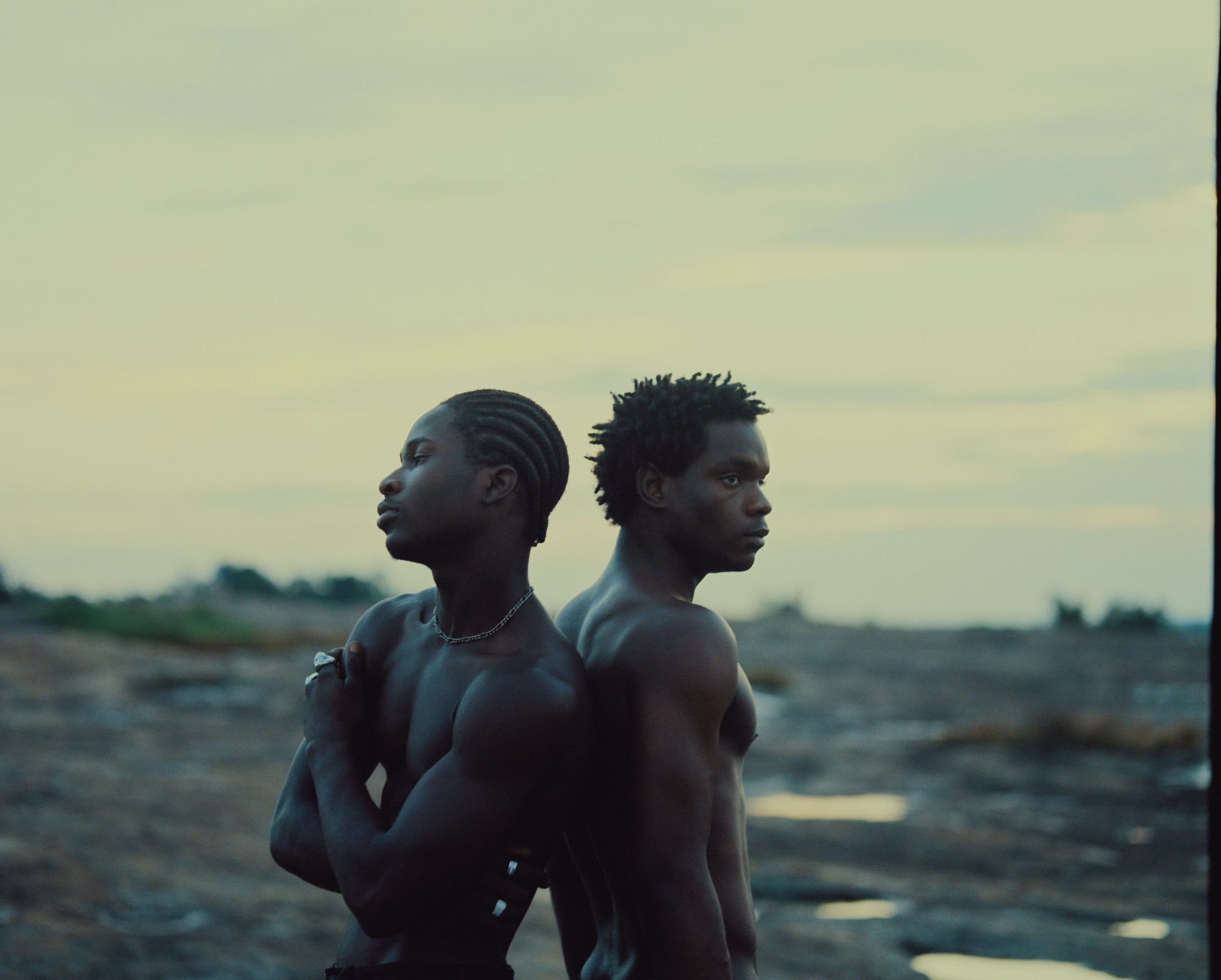 two shirtless men standing back to back