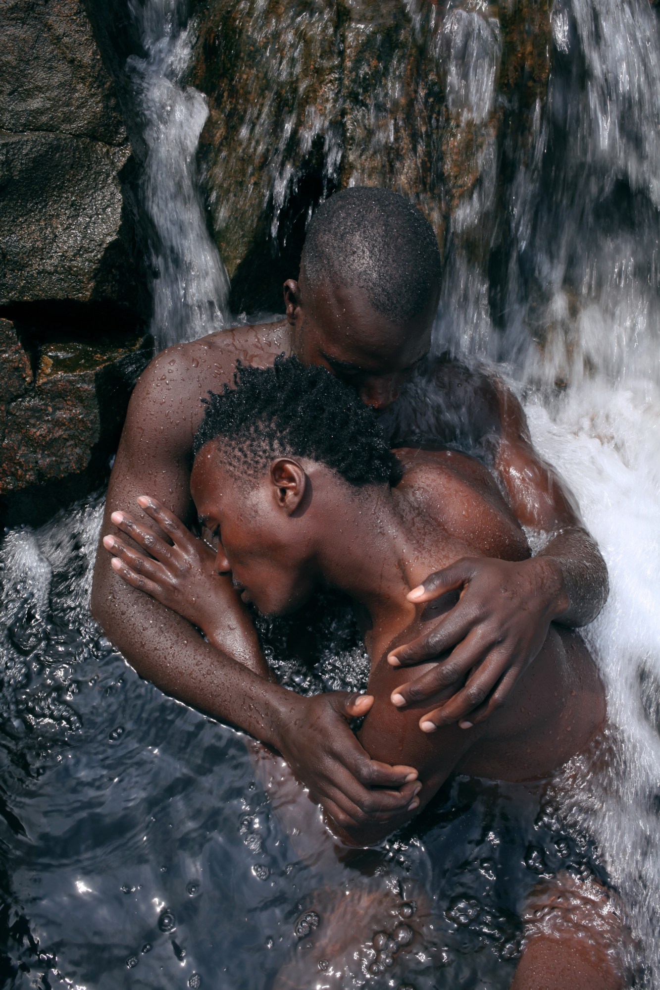 two men holding each other in a waterfall