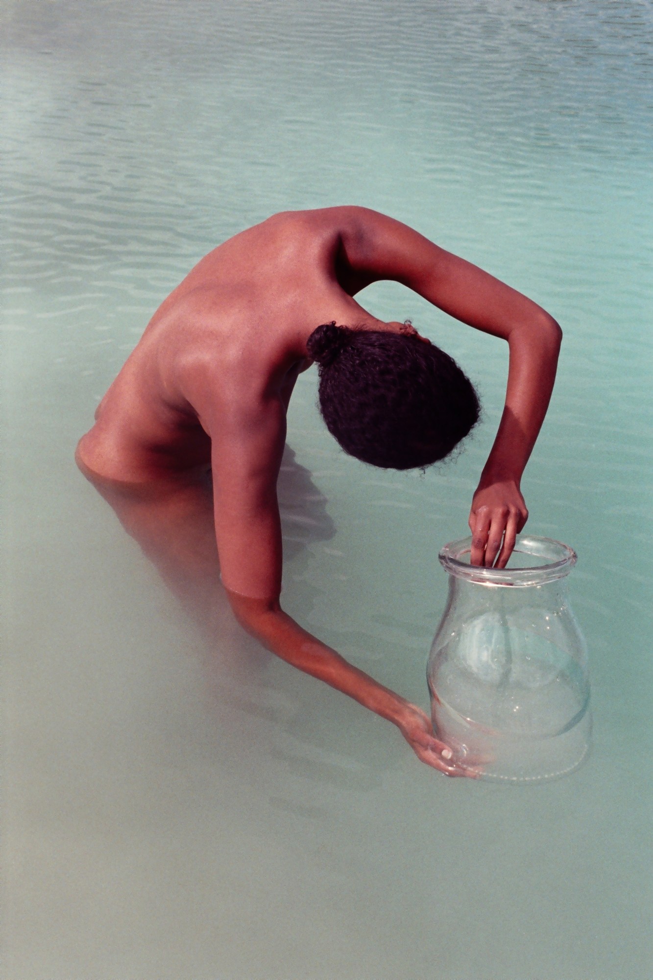 a woman stood in misty turquoise water holding a glass vase