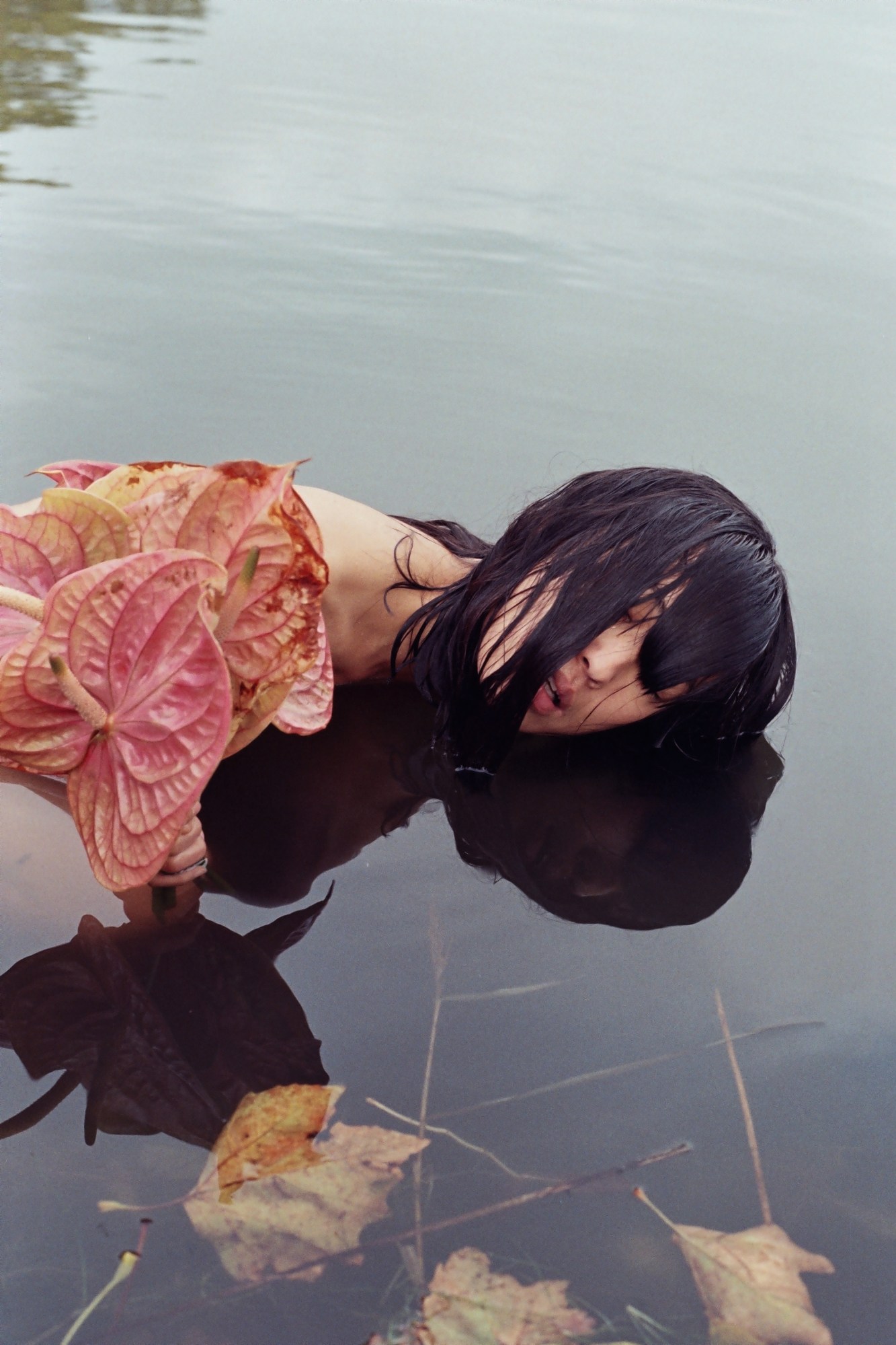 a woman drops her hair into a body of water with leaves and flowers in it