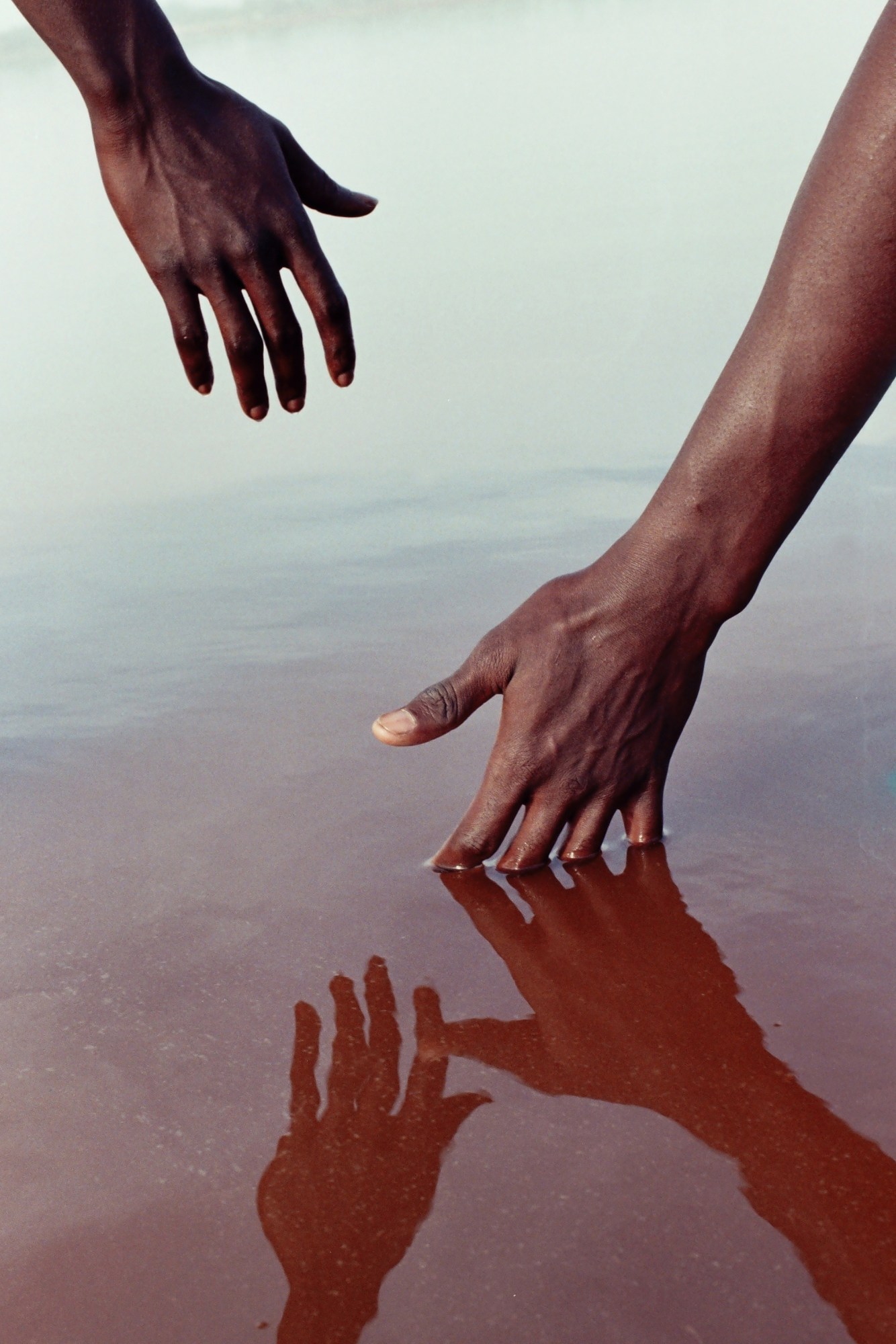 two hands outstretched over dark red water