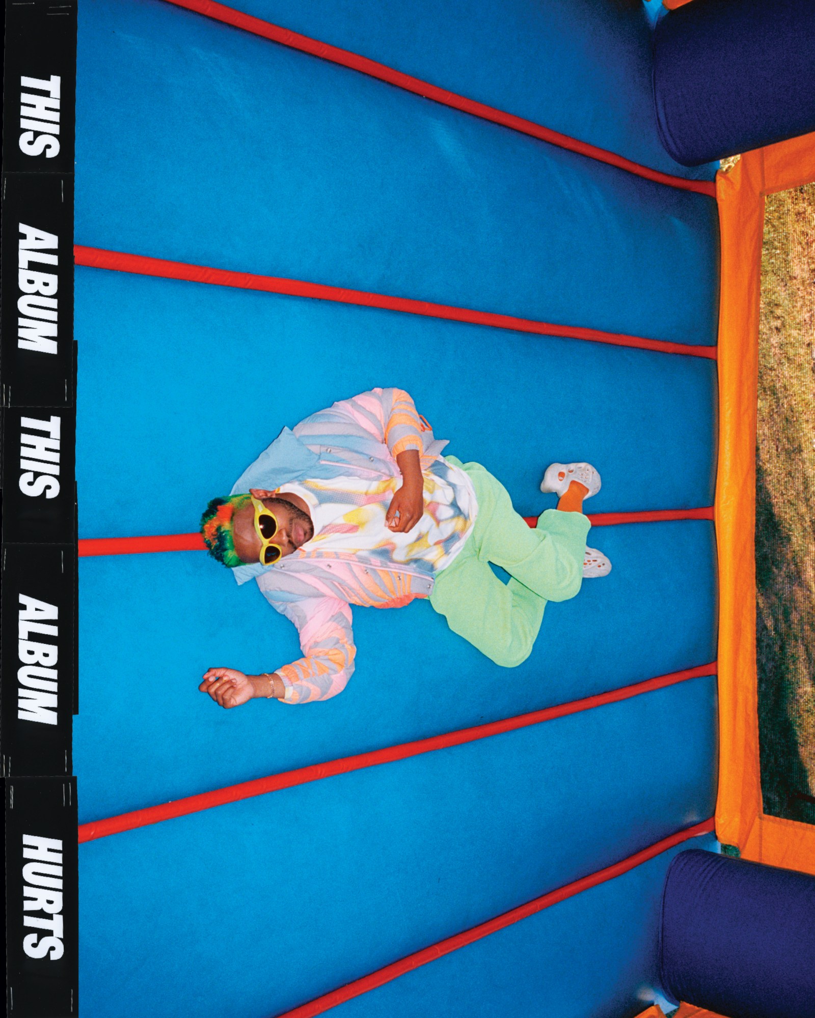 an image of Kevin Abstract laying on a blue bouncy castle wearing colourful clothes