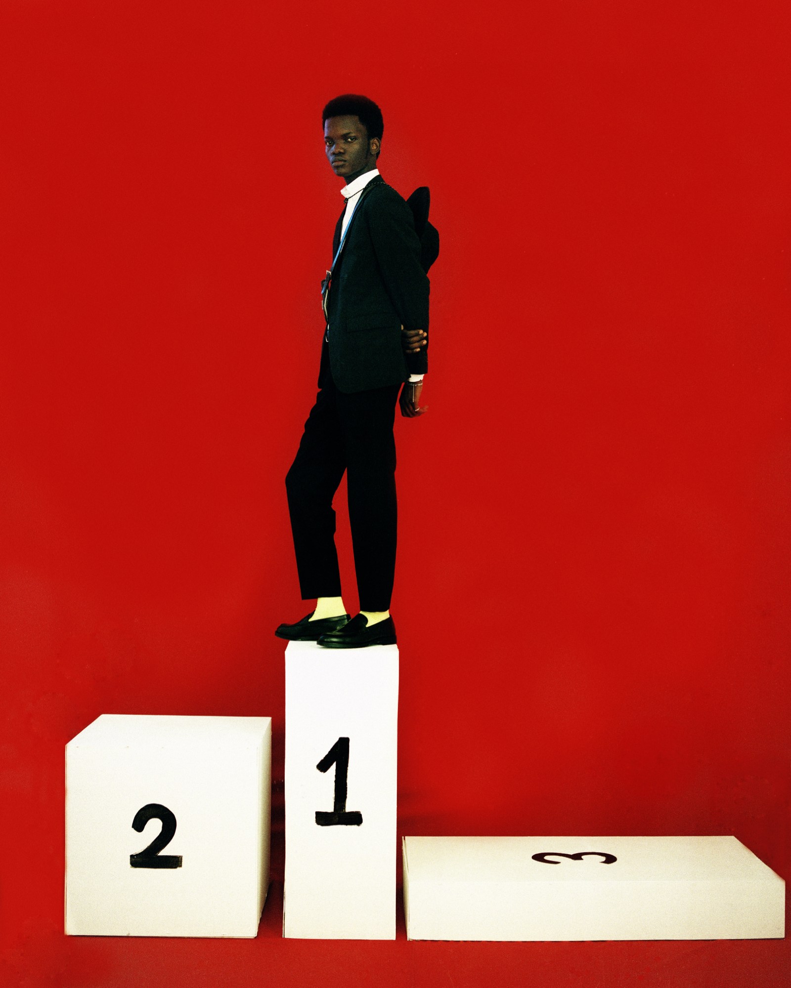 a man wearing a suit stands on a podium that has number 1 written on it, either side are 2 (left) and 3 (right)