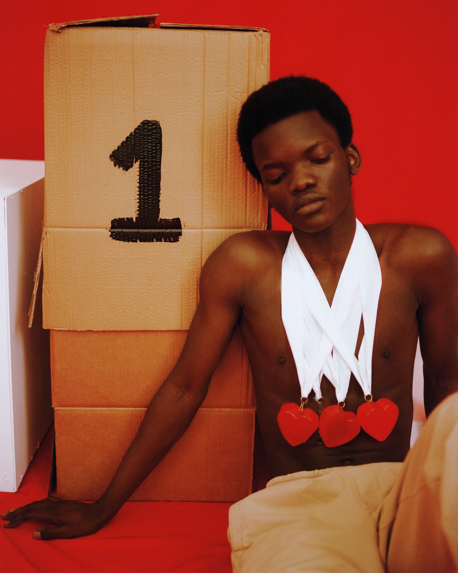 a man wearing homemade medals and no t-shirt rests against a box with the number 1 on it