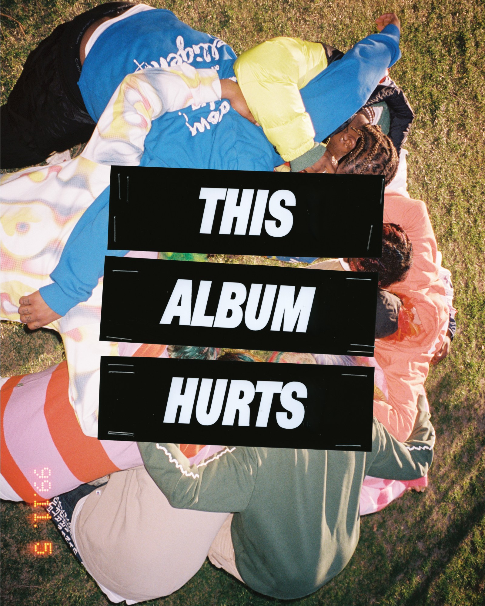 Brockhampton members with their arms around each other in a circle looking down at the grass, from above