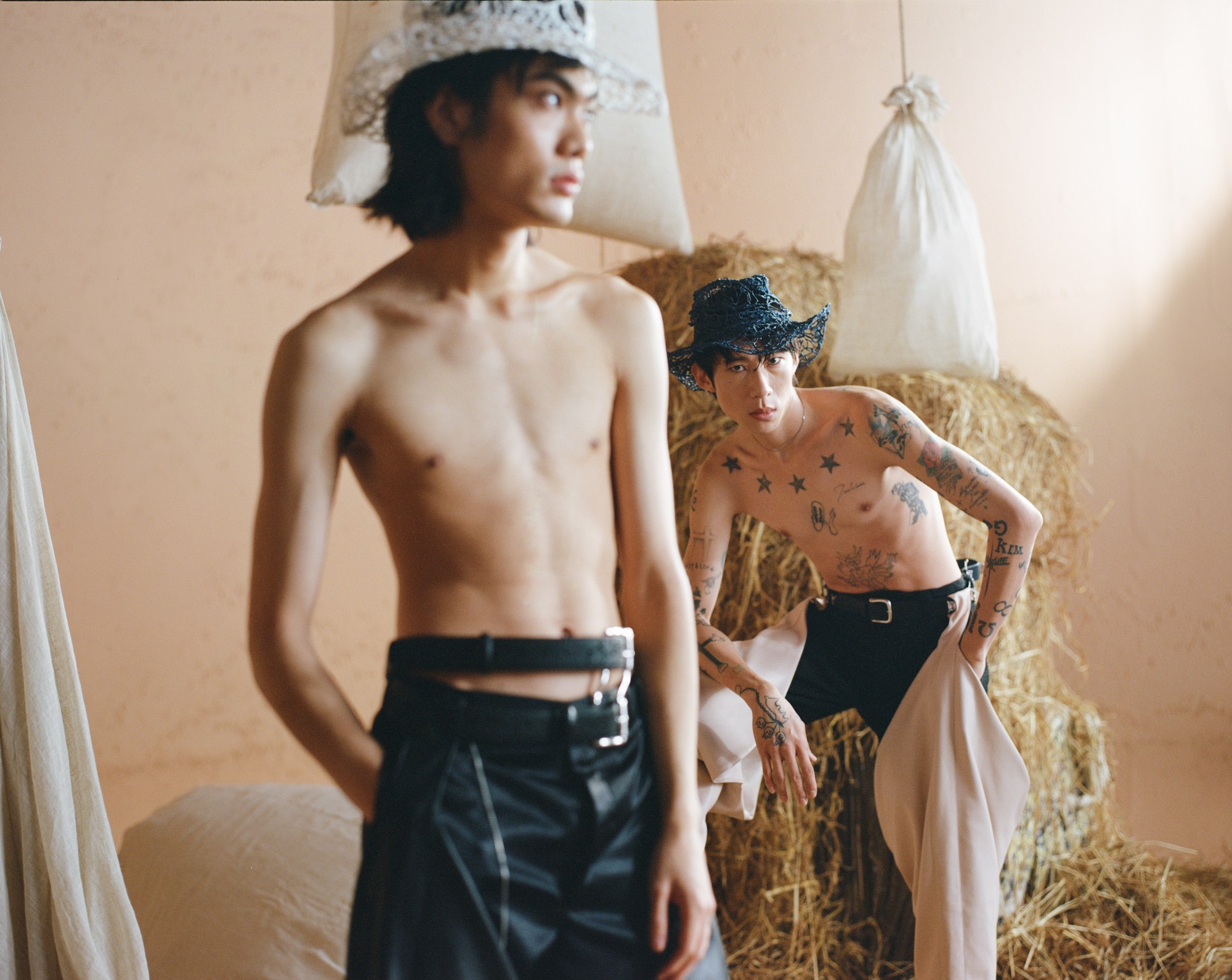 Two models wearing black Ponder.er trousers and woven cowboy hats, with hay behind them.