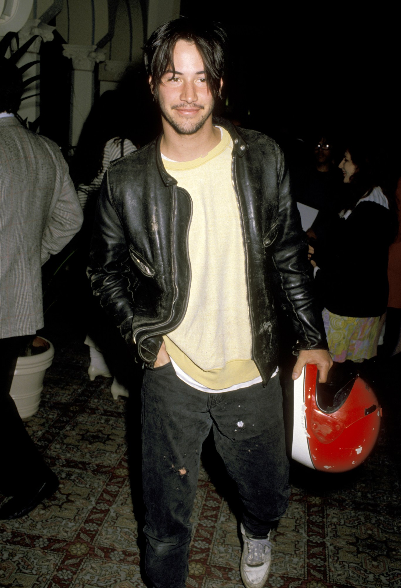 keanu reeves in a leather jacket and holding a motorcycle helmet on the red carpet