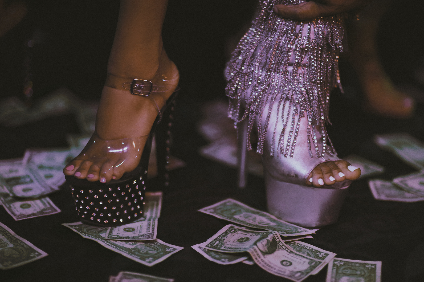 two bejewelled stiletto heals standing on a carpet of dollar bills