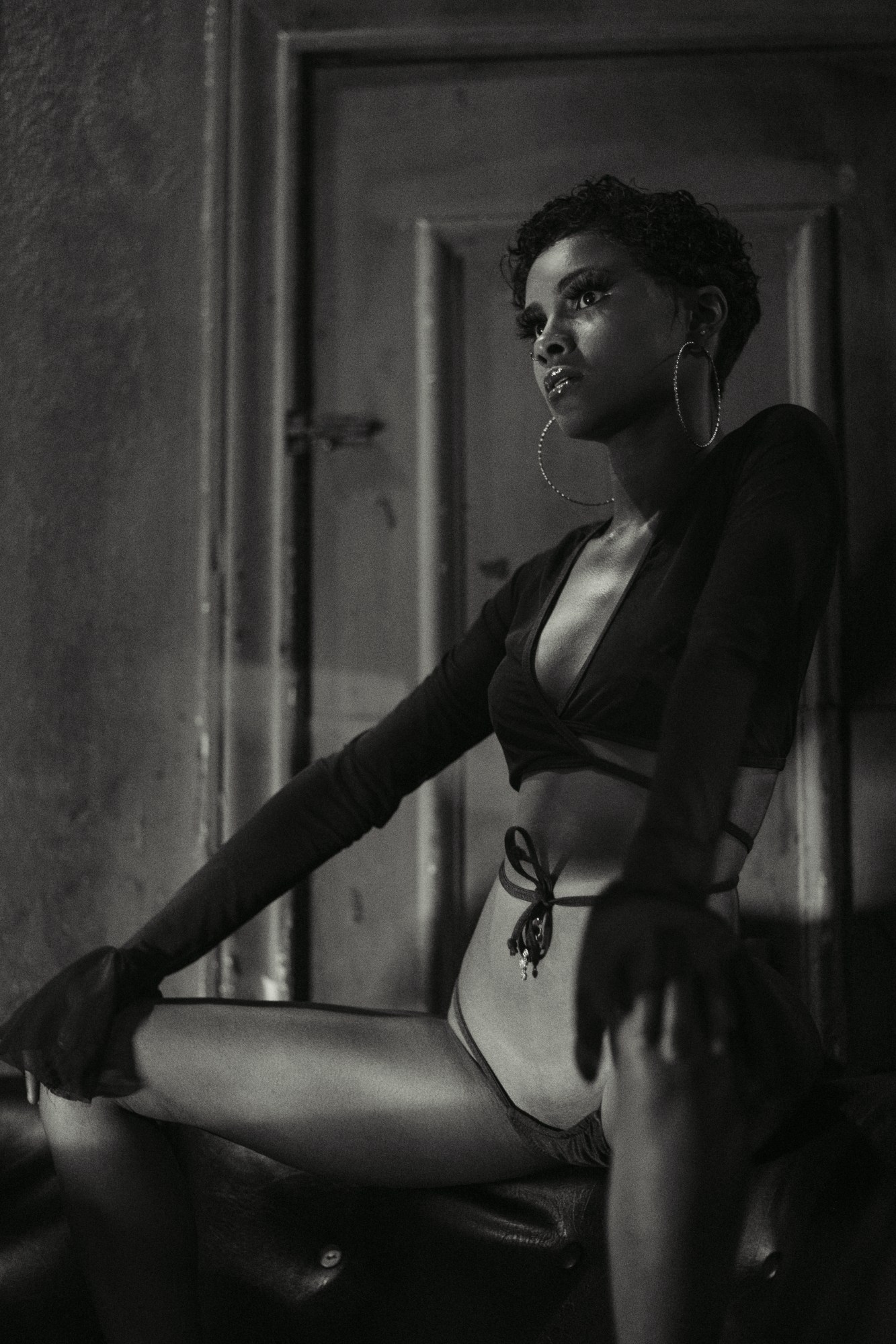 a black-and-white image of a a woman in underwear and large hoop earrings, sitting with her legs apart